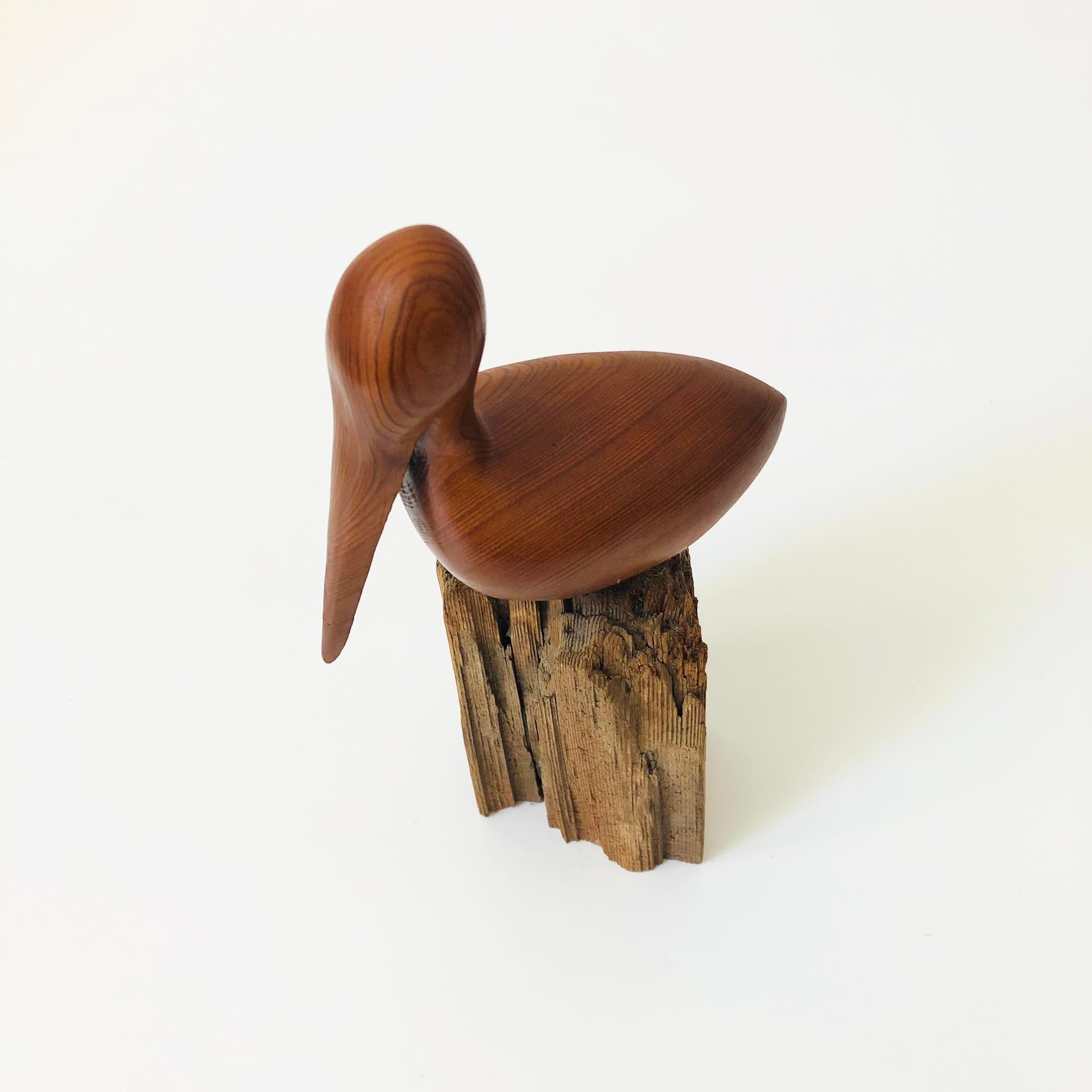 A vintage carved wood pelican. Made of teak that has been carved smooth and mounted on a contrasting natural driftwood base. Nice simple minimalist shape. Signed on the base 