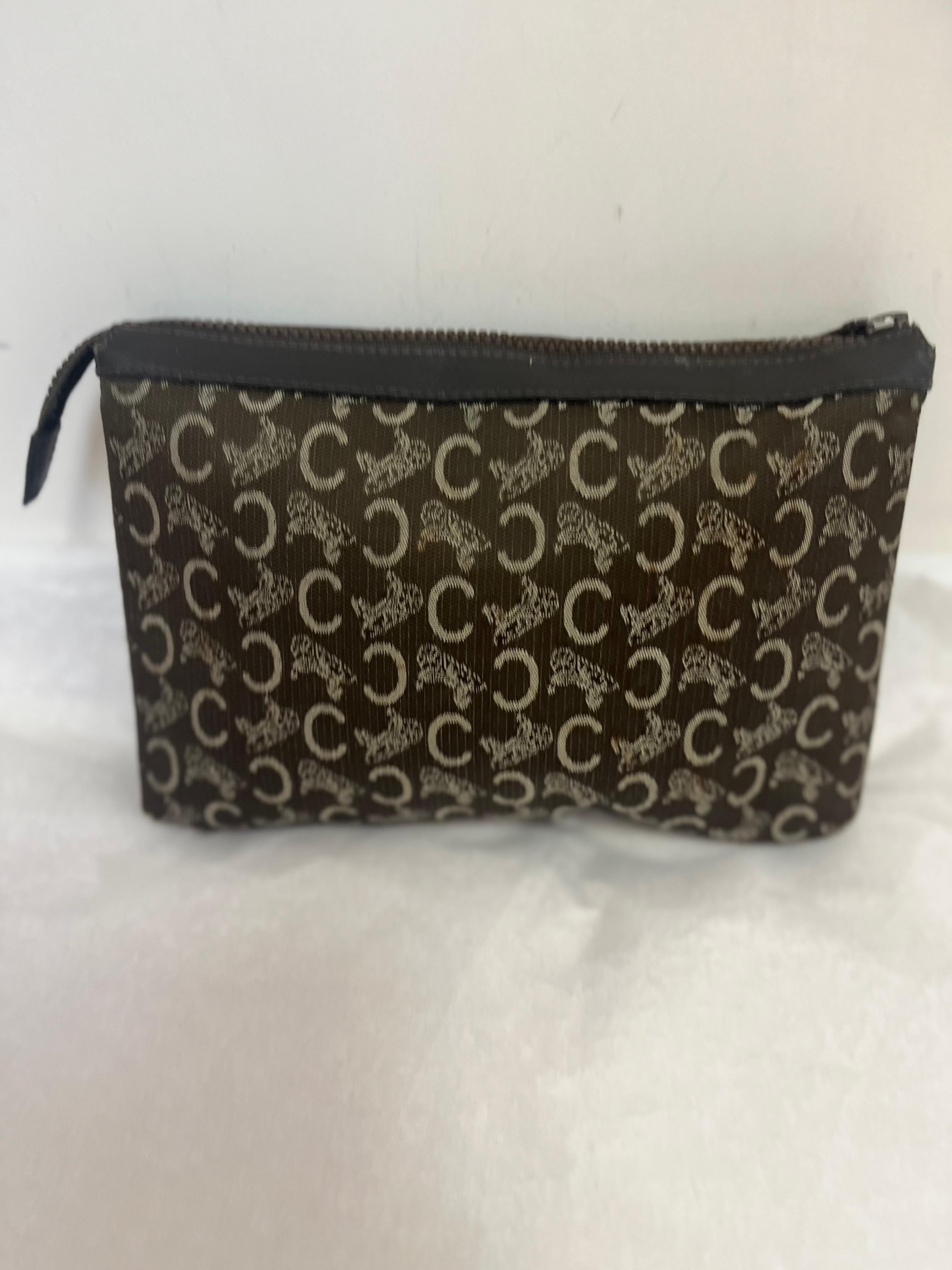 This is a Celine clutch with the original Presbyopia monogram pattern, inspired by the Arc de Triomphe in Paris. The clutch has a top zip closure and a black leather lining.
The escutcheon on the front features the name Celine and a horse a