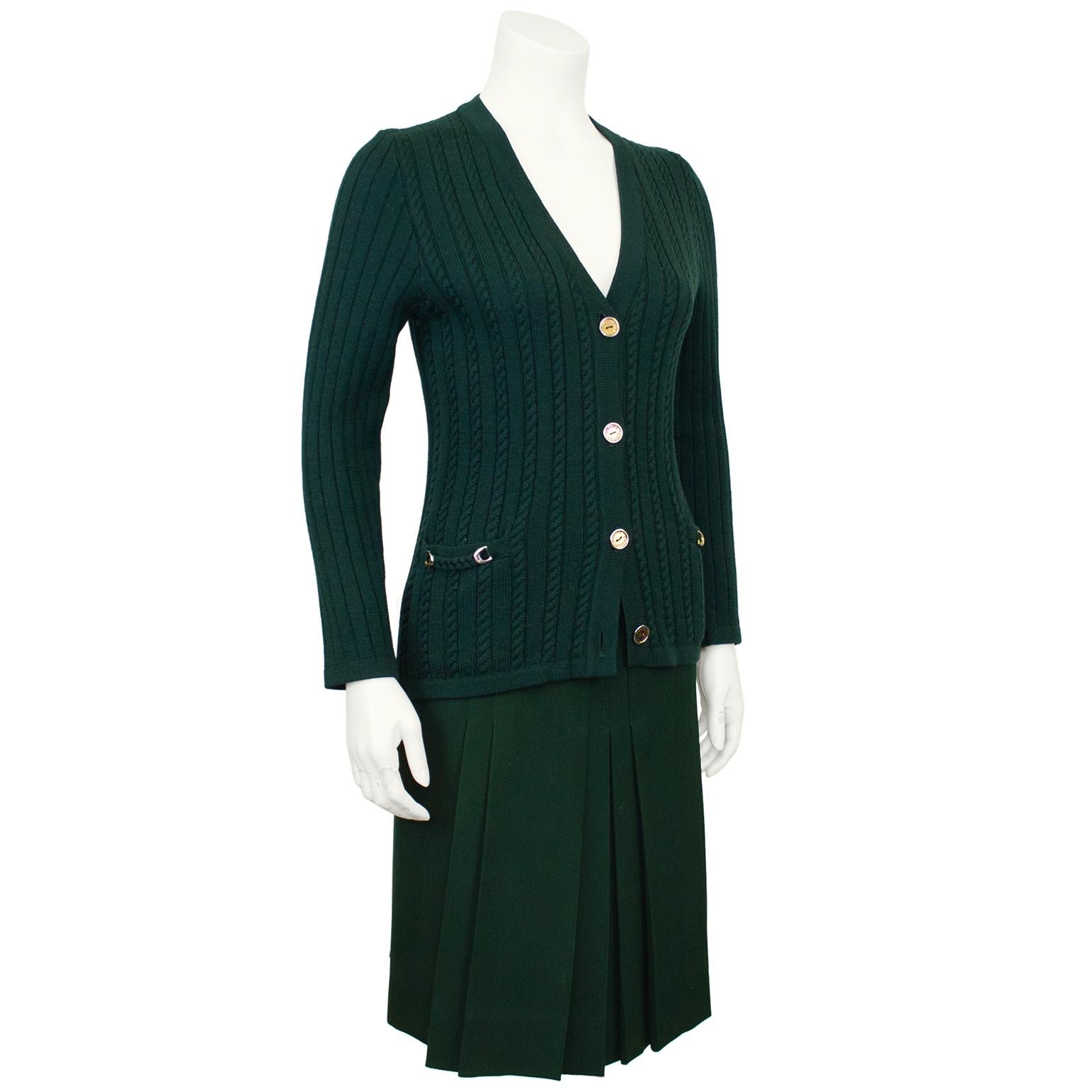 Classic and timeless Celine 100% wool forest green cardigan and gabardine skirt ensemble from the 1970's. The set features a cable knit v neck cardigan with gold tone metal accents. Slit pockets at the hips with horse bit details. The pleated skirt