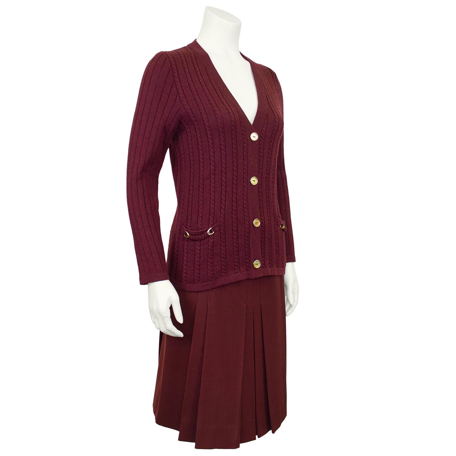 Classic French girl style, Celine 100% wool maroon cardigan and matching gabardine skirt ensemble from the 1970's. The set features a cable knit cardigan with braided trim at the pockets with gold tone horse shoe details. The pleated skirt is high