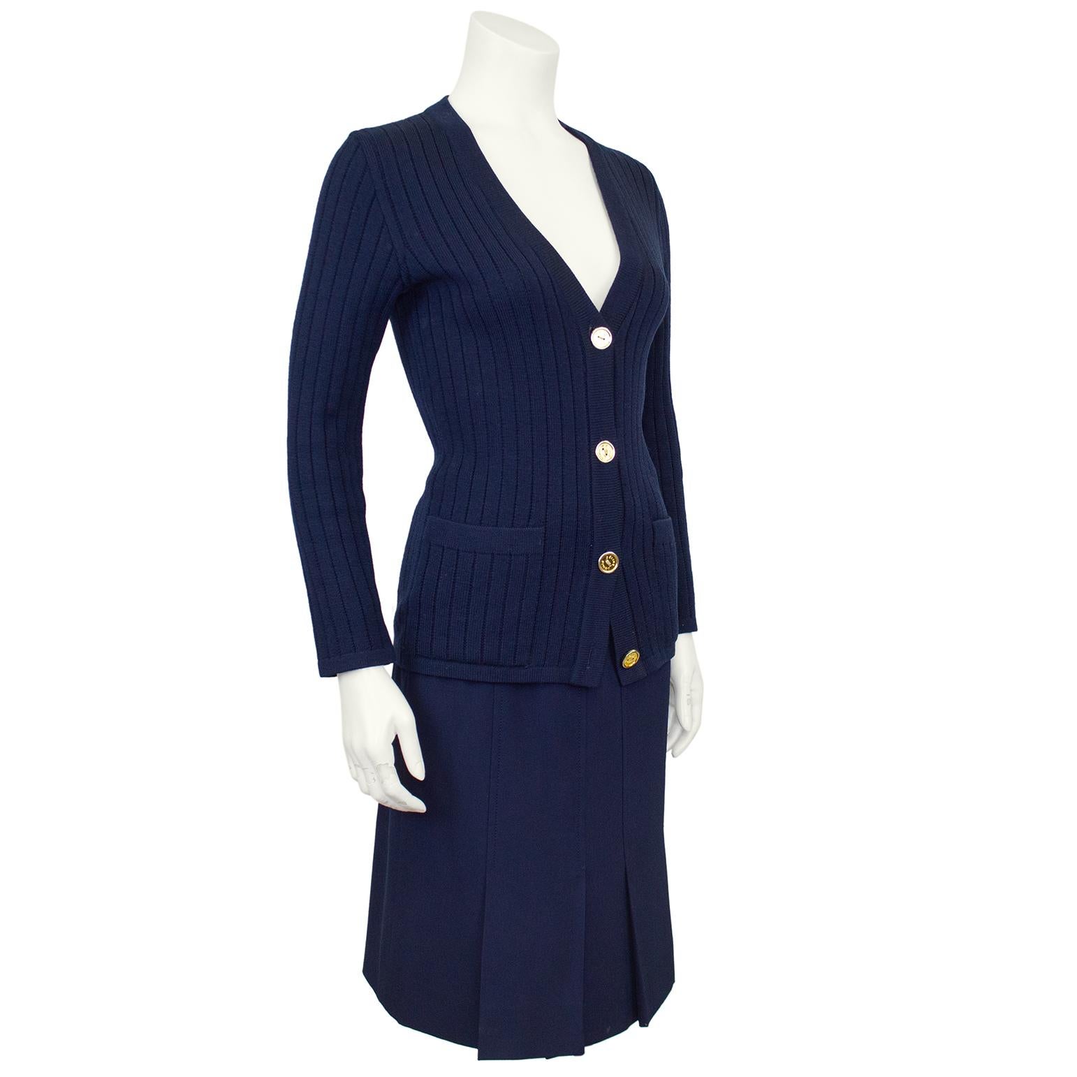 Classic and timeless Celine 100% wool navy blue cardigan and gabardine skirt ensemble from the 1970's. The set features a ribbed v neck cardigan with gold tone metal accents. Slit pockets at the hips with beige embroidered logo on the left hip and