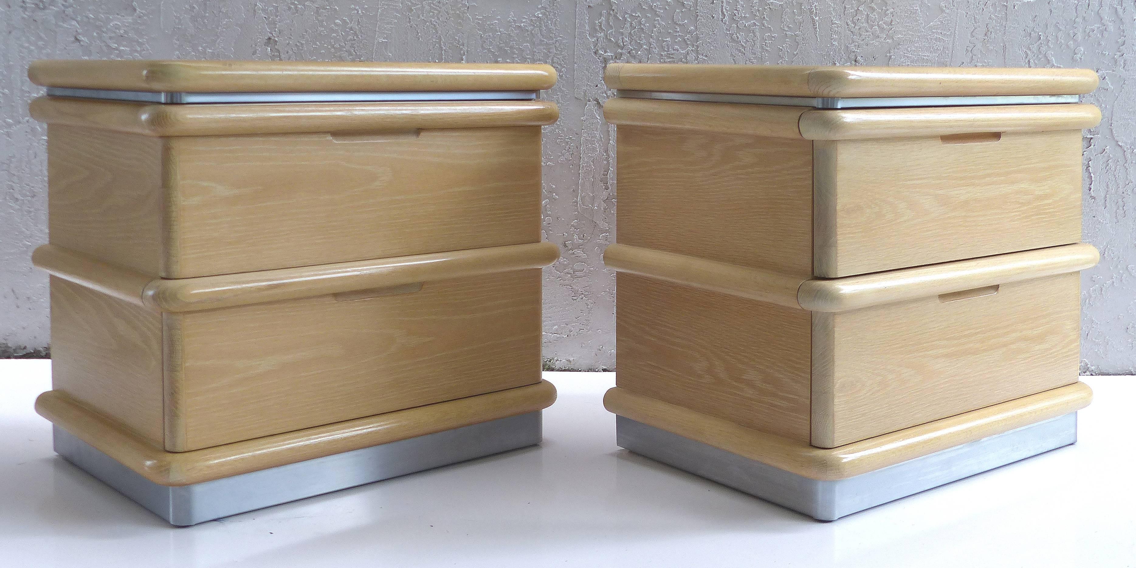 Offered for sale is a pair of circa 1970s cerused wood nightstands with brushed steel bases and trim by Jay Spectre for Century Furniture. The cabinets each have two drawers with rounded wood banding and each is signed within the top