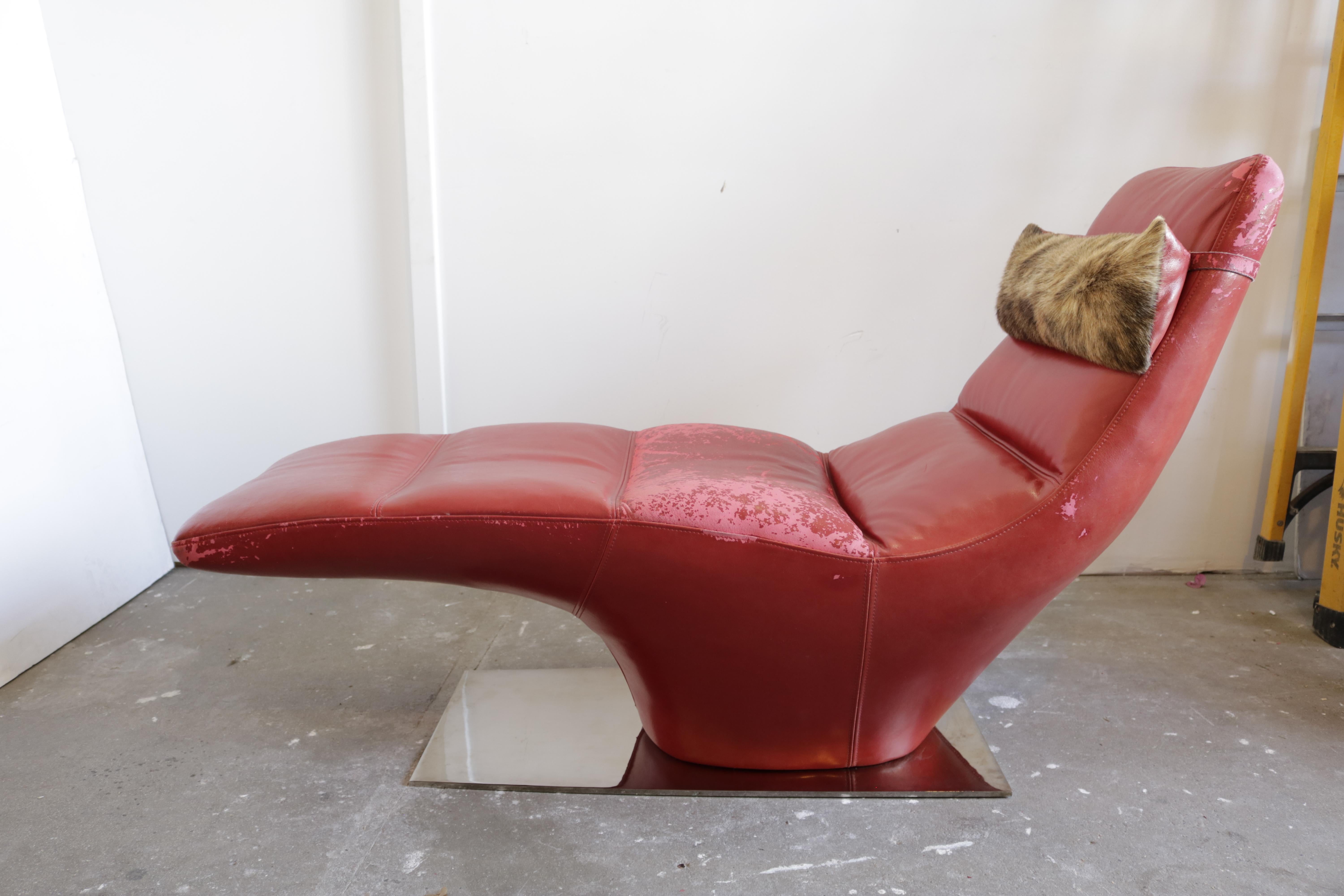A vintage distressed red chaise longue with detachable faux fur accent. 
It sits on a chrome base.
Obviously, it needs a new upholstery. We can make it done if you send your fabric.