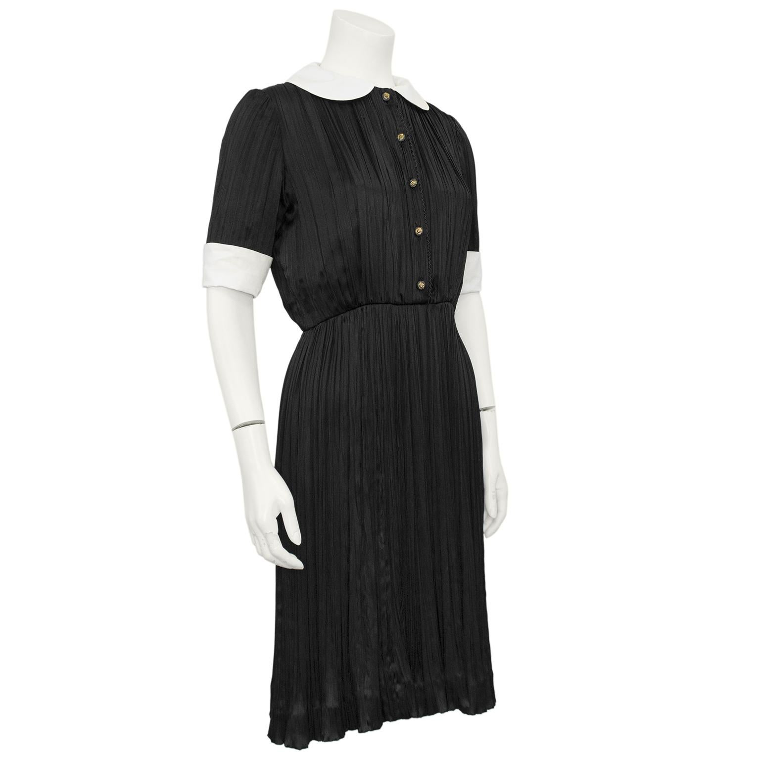 Very sweet 1970s Chanel Creations short sleeve shirtdress. Micro pleated black silk with removable white cotton Peter Pan neckline and cuffs. Black and bronze tone lions head small buttons and twisted silk rope trim down the centre of the bodice.