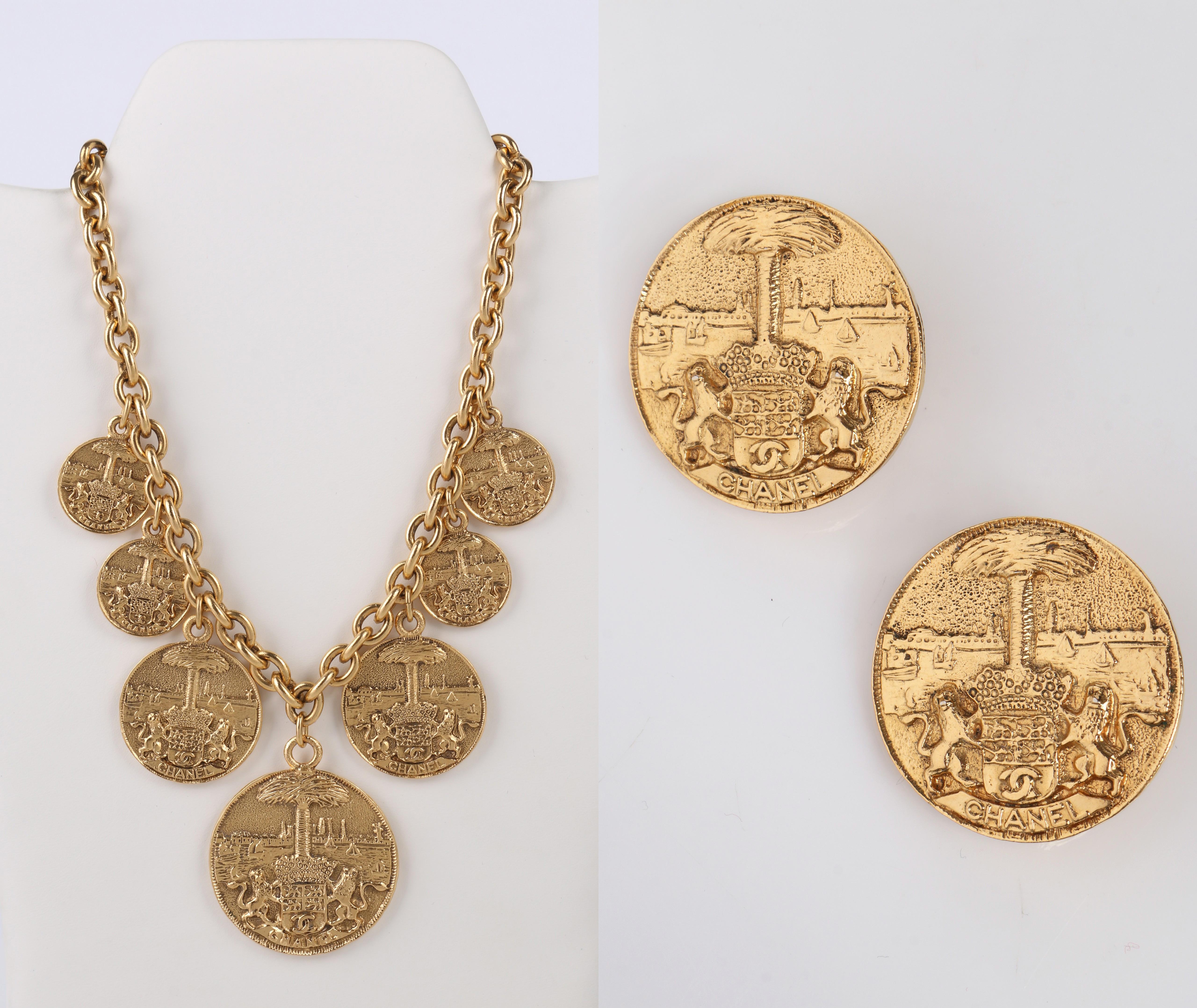 Vintage 1970's CHANEL Coat of Arms / Crest gold tone medallion necklace and matching clip on earrings.  Large gold tone medallions have detailed engraving of seaside view with sailboats on water in background, with large palm tree in center and two