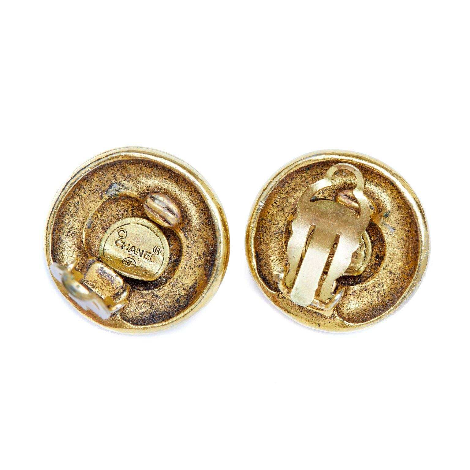 These classic Chanel 1970s or early 1980s gold earrings are of superb quality and condition. An oversized round cut rhinestone encased at the centre of each piece is surrounded by a rope motif in gold plated metal. There are clip-on fastenings at