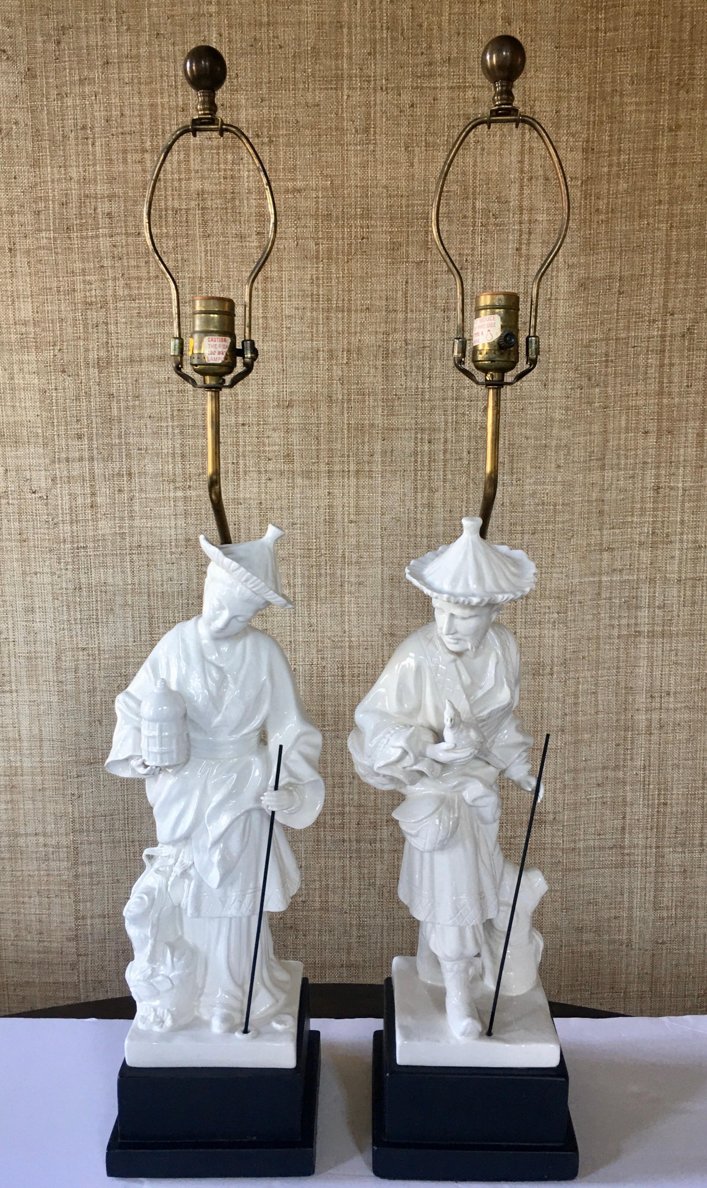 Pair of midcentury chinoiserie figural table lamps by Chapman. These beautifully detailed Hollywood Regency style lamps feature glazed cream porcelain figures mounted on black plinth bases. Lamp shades not included.

Measures: Lamp height to