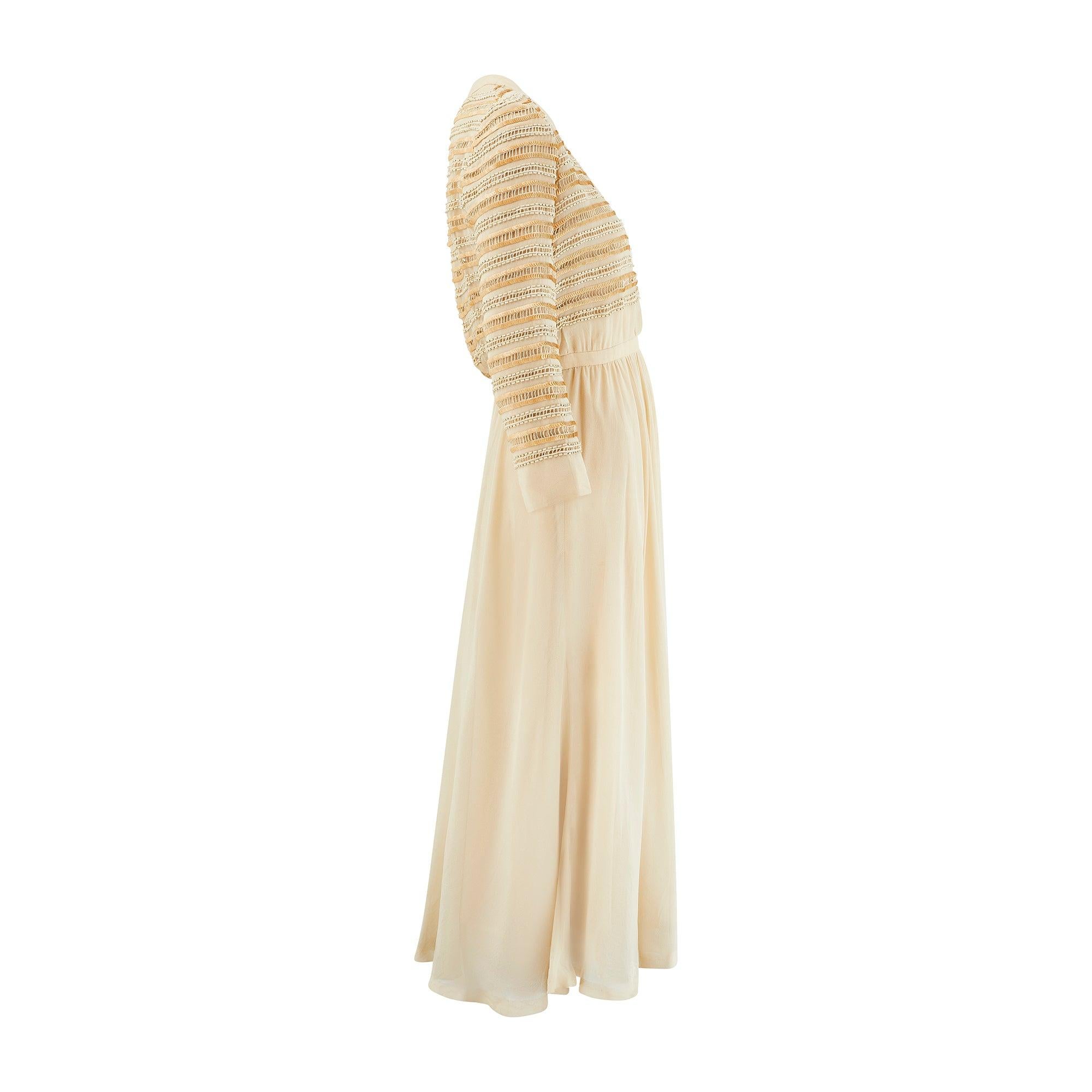 Este elegante vestido de noche fue diseñado por Christian Dior en la década de 1970 y lleva la etiqueta de una sucursal londinense. Vestido midi de manga larga confeccionado en la más fina gasa de seda semitransparente de color caramelo. La falda