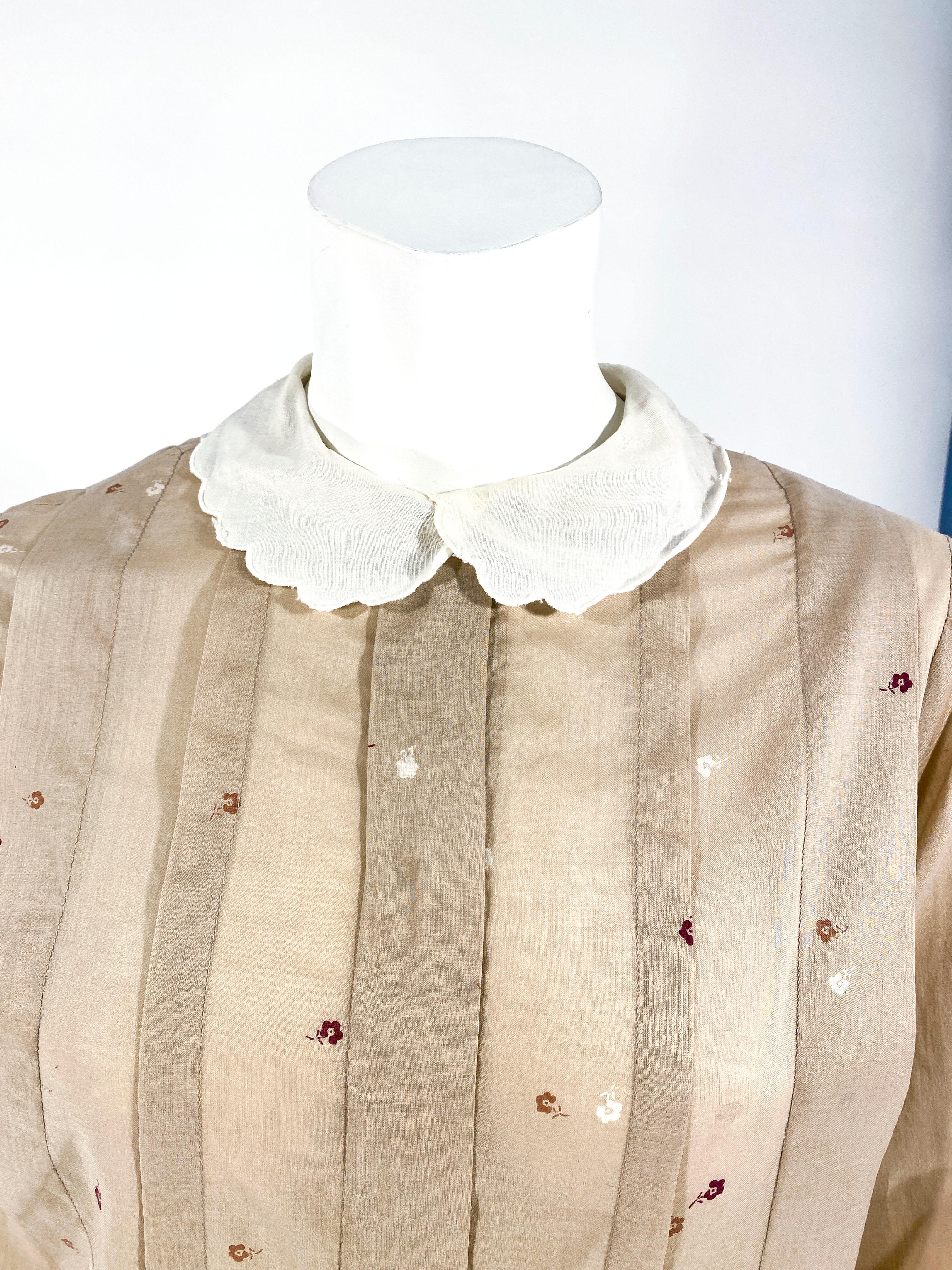 1970s Christian Dior cotton printed blouse with large knife pleats on the face of the garment, full pleated sleeves, and a scalloped peter-pan collar. The print is a vintage floral pattern with touches of maroon, tan, and cream colored flowers.