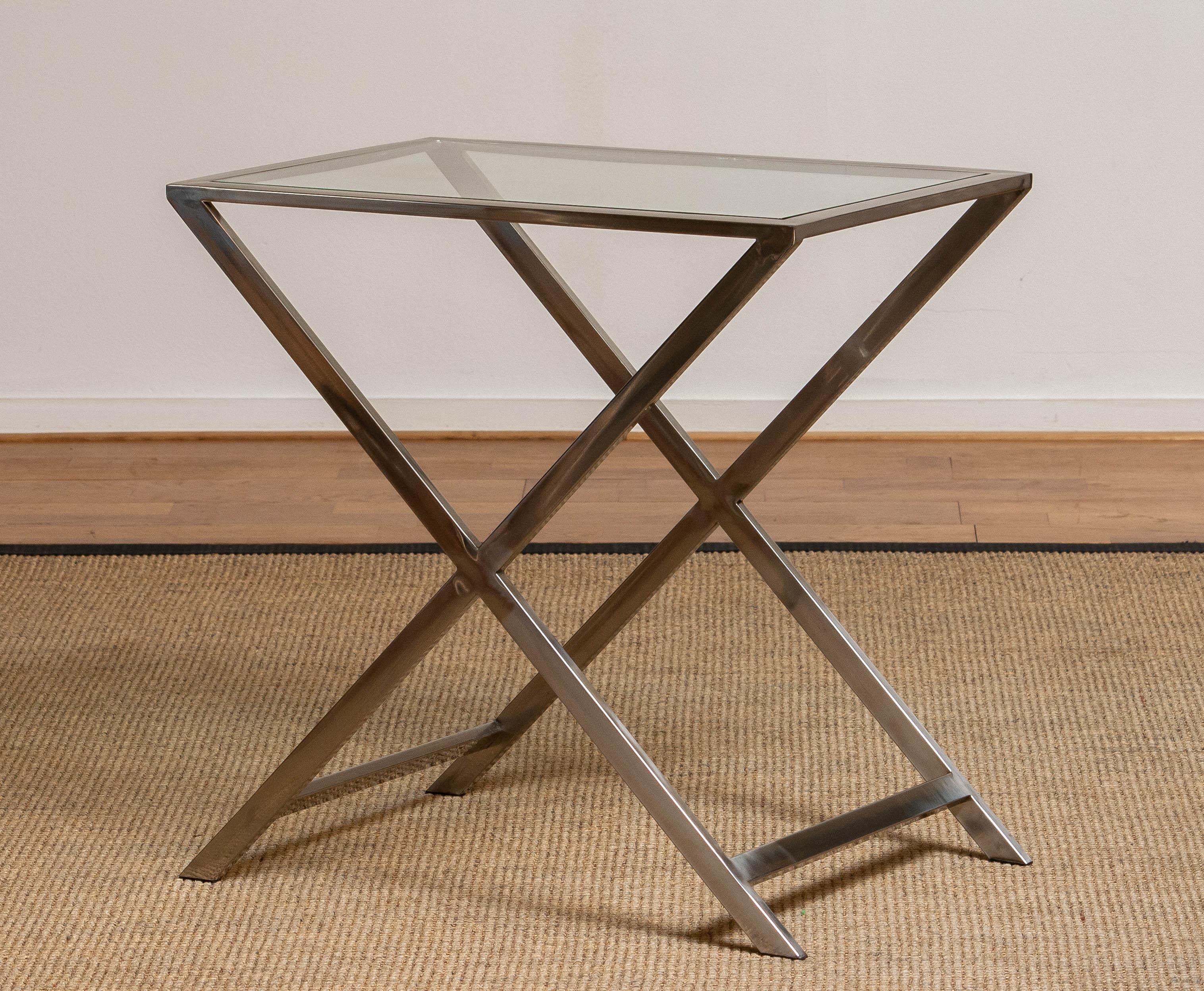 Ein schlichter und eleganter Beistelltisch aus den 1970er Jahren mit einem minimalistischen X-förmigen Chromgestell und einer klaren Glasplatte. Die klaren Linien und spiegelnden Oberflächen verleihen ihm eine zeitlose, modernistische Ausstrahlung