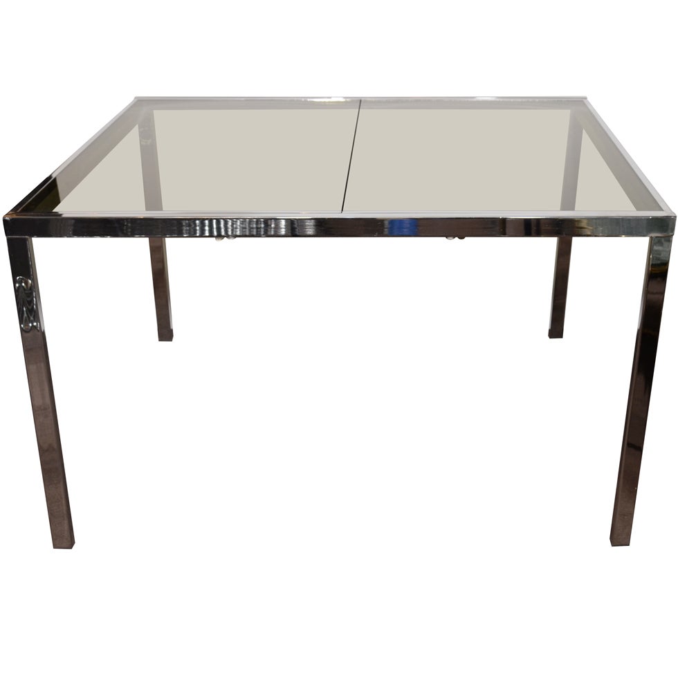 Design Institute of America, Mid-Century Modern dining table with streamline design in chrome and with smoked glass top and inset leaf. Features built-in smoked glass extension which raises flush to the table by unlocking underside latch and pulling