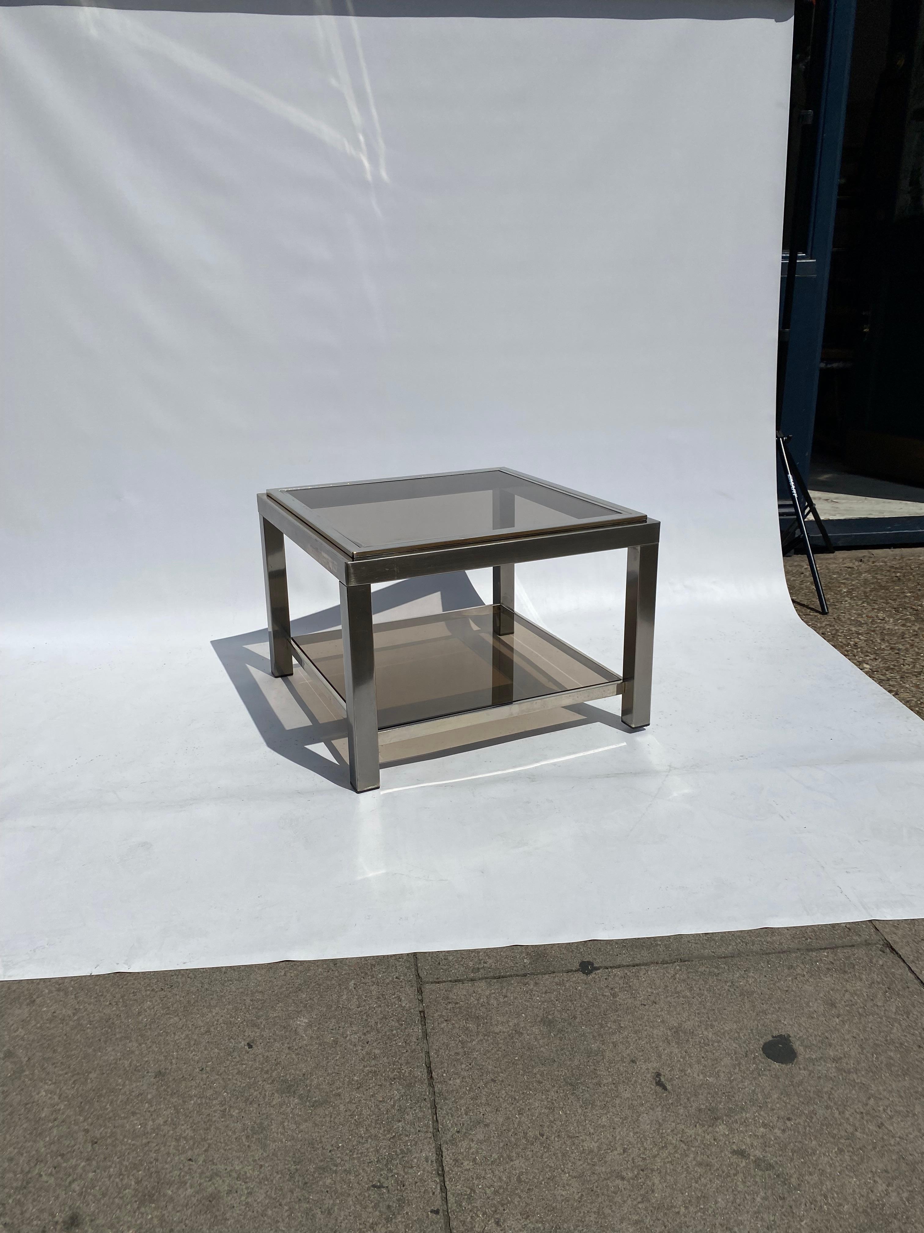 A stylish 1970s two tiered side in aluminium steel frame and smoked glass.
This square table is very much in the style of the ones of Willy Rizzo and Jean Charles, although lake a signature it doesn't disappoint on quality. Steady and masterfully