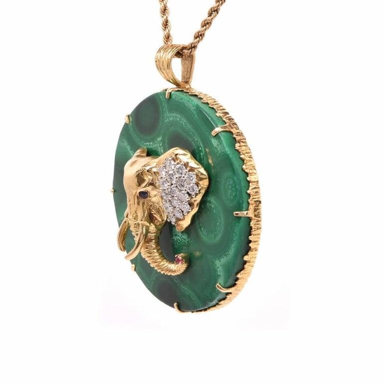 This vintage  circular pendant circa 1970's pendant  is made of solid 18k gold frame with malachite Stone. Enriched with an elephant head with pave set diamond ears, sapphire eyes and a ruby on her trunk. 
Elongated yellow gold prongs and a wide