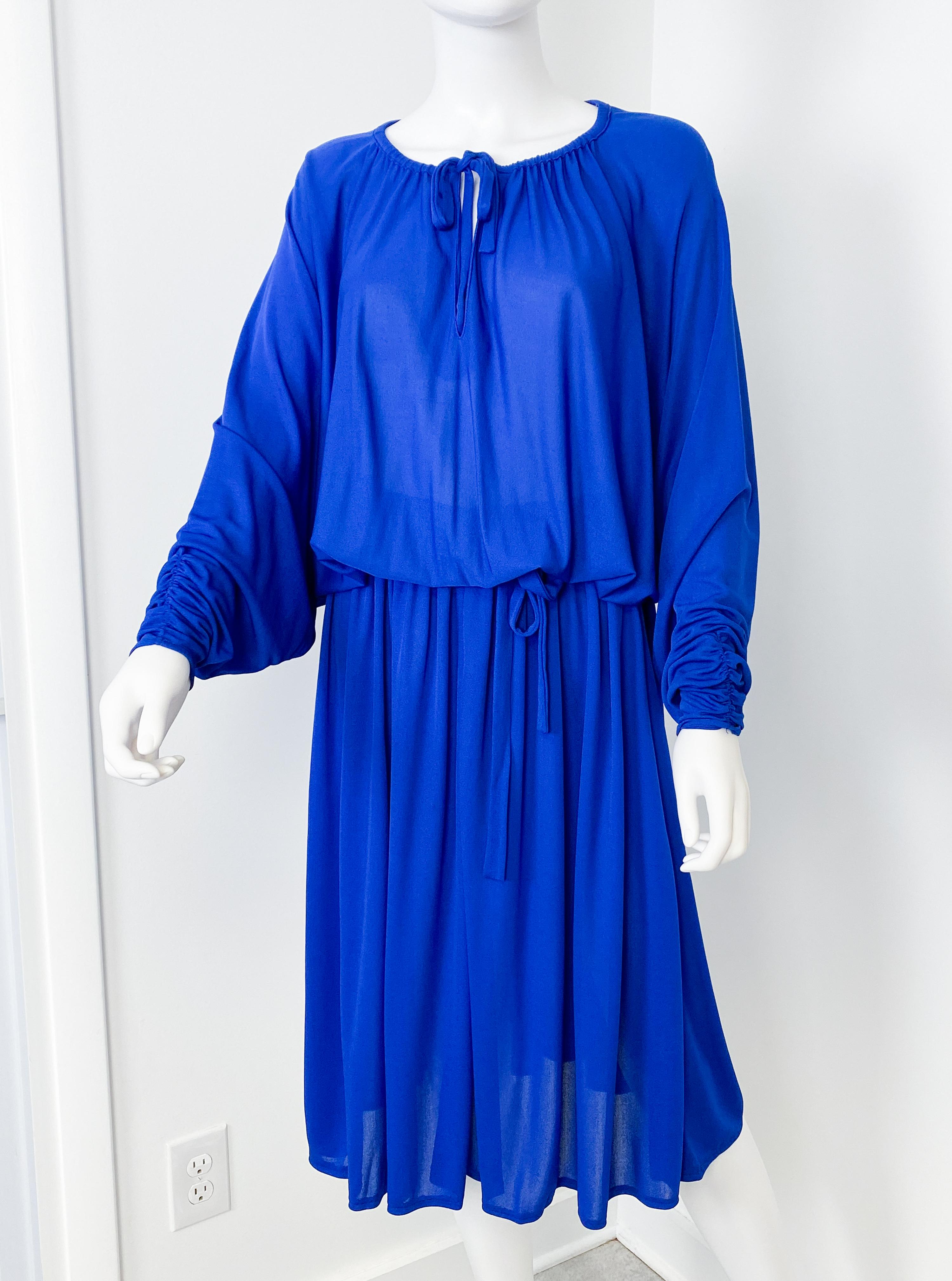 Cette exquise robe de cocktail vintage des années 1970 est une véritable pièce d'apparat d'un bleu cobalt radieux. Confectionné en jersey doux et légèrement transparent, il se drape merveilleusement, créant une silhouette fluide sans effort.