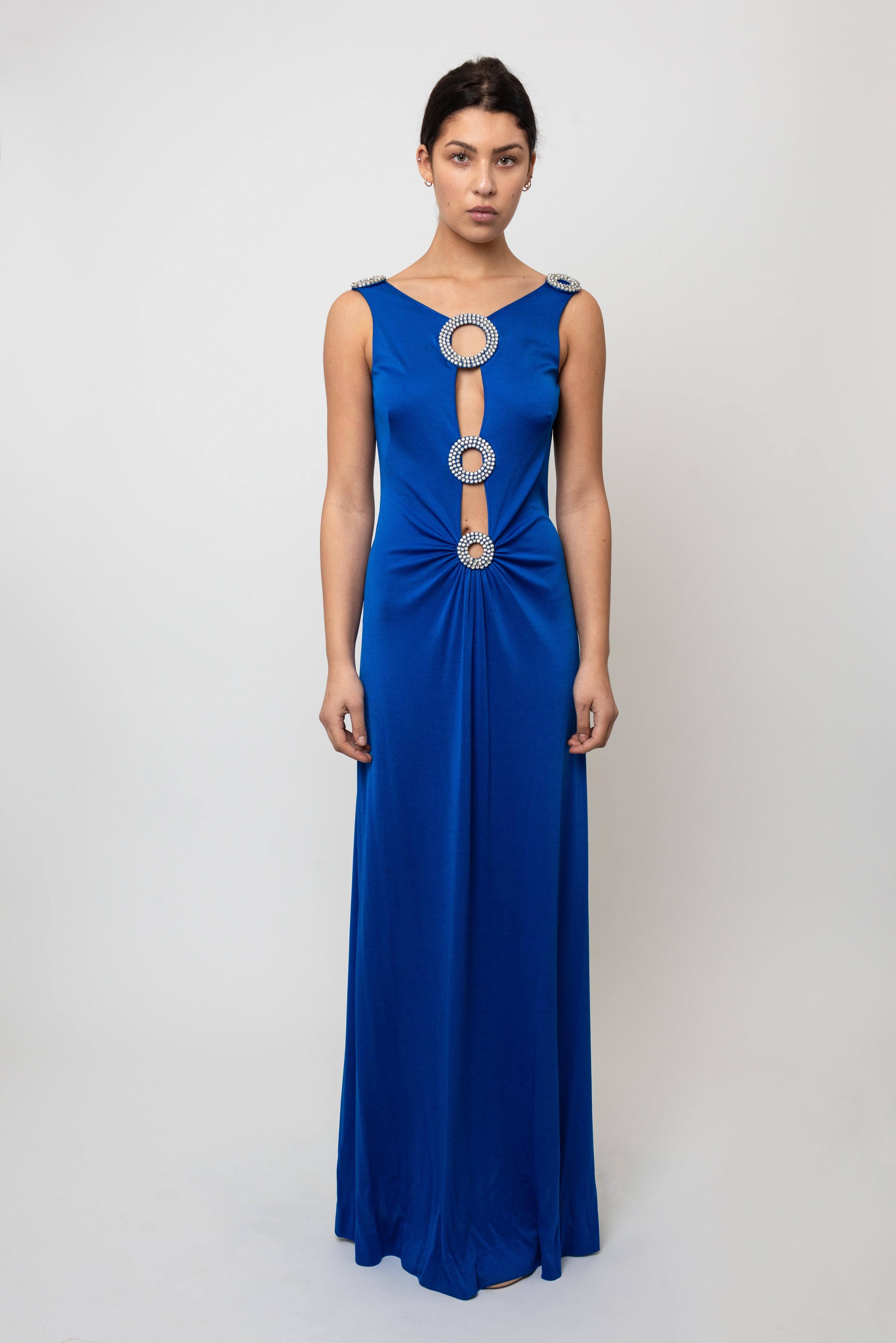 Step into the disco fever of the 1970s with this stunning Loris Azzaro jersey gown, a true Studio 54 showstopper. Rendered in rich cobalt blue, this glamorous piece features strategic cut-outs adorned with sparkling crystal trim that catches light