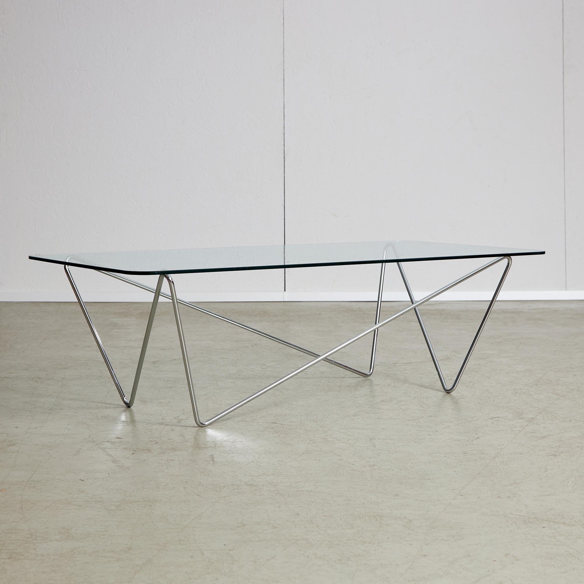 This coffee table, which comes from the 1970s, has a slim chrome frame that is designed in a zig-zag pattern. This frame holds up a thick piece of tempered glass on top. The glass is strong and can resist scratches and spills, which helps keep the