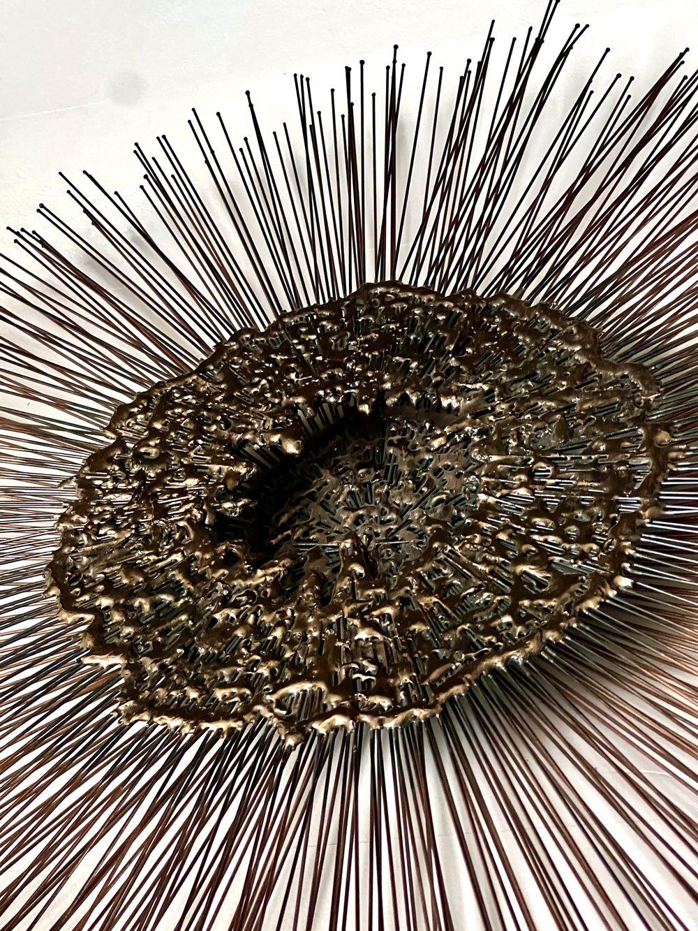 Inspired by the styles of Curtis Jeré & William Friedle Bruce, and crafted with precision, this vintage wall relief showcases a central three-dimensional brass orb, surrounded by torch-cut copper-toned iron wire in varying lengths. Sunburst rays