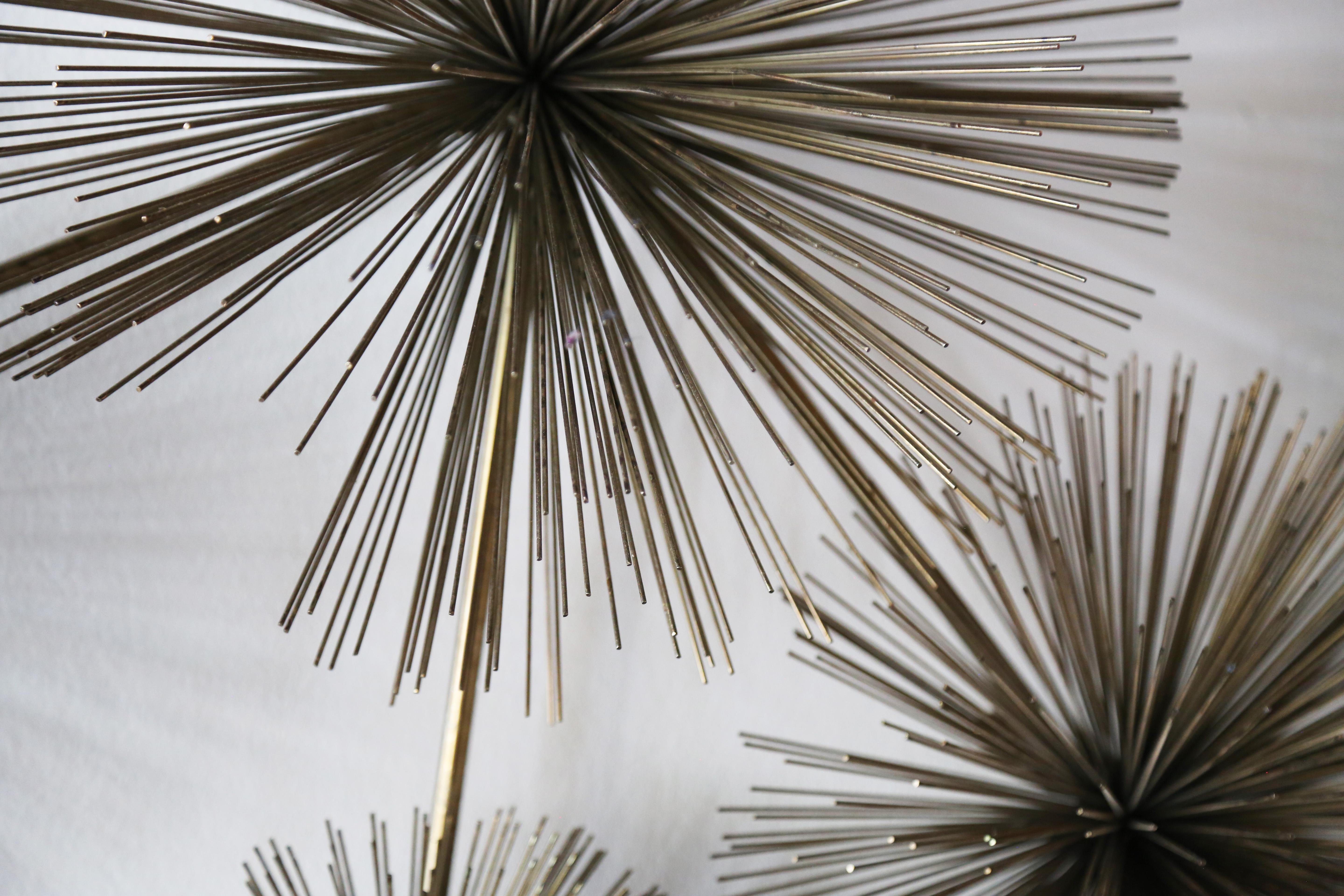 An urchin shaped, sunburst pom pom wall sculpture by Curtis Jere. Signed and dated 1979. An iconic mid century look of 5 urchins of varying sizes which provides depth and texture and visual interest to any surface. All original brass colored metal.