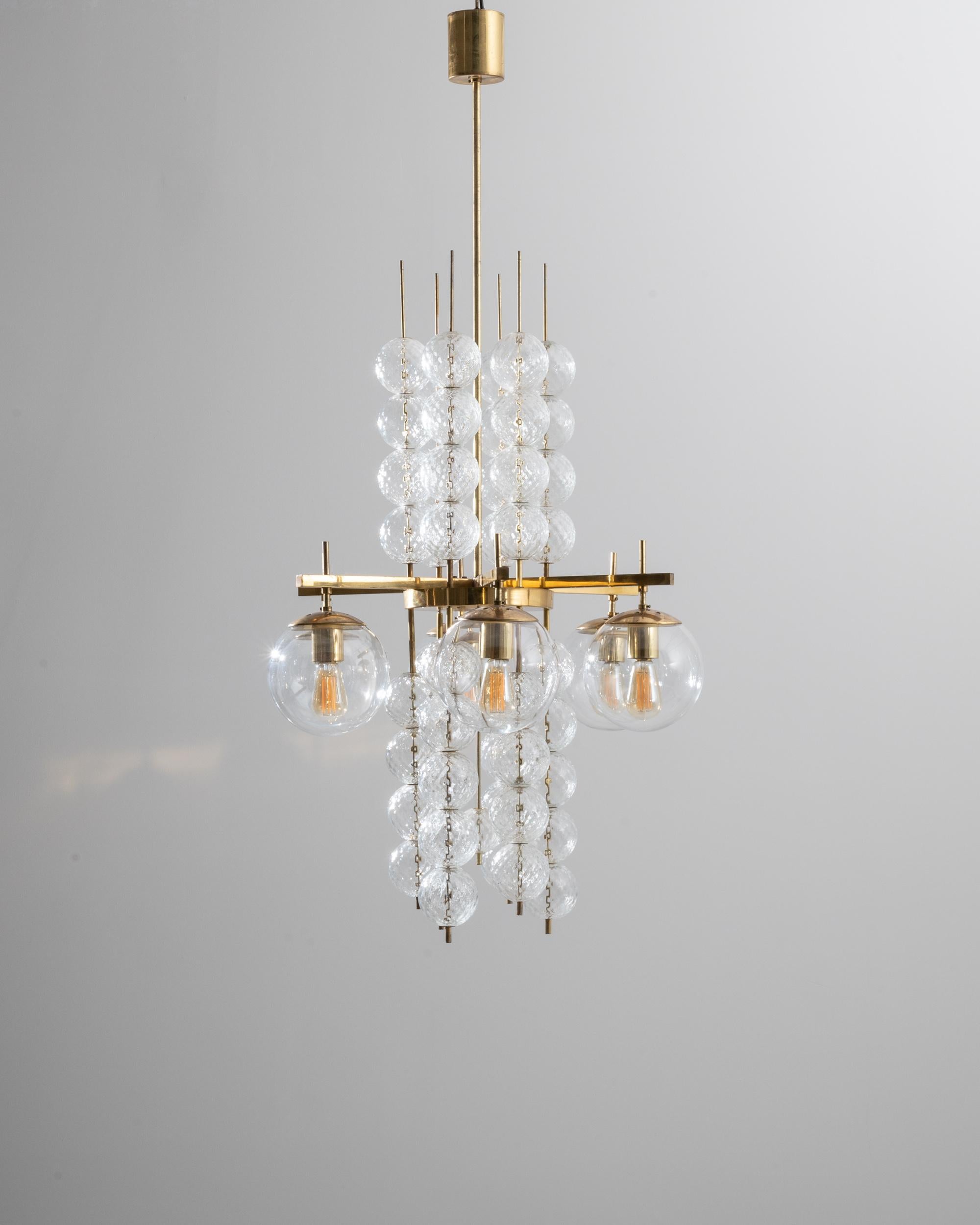 A 1970s brass and glass chandelier from Czechia, this astonishing lighting piece is composed of gilded tubing and canopy, supporting a busy assemblage of translucent glass spheres. The cross structure bears four elegant bulbs encased in plump orbs,