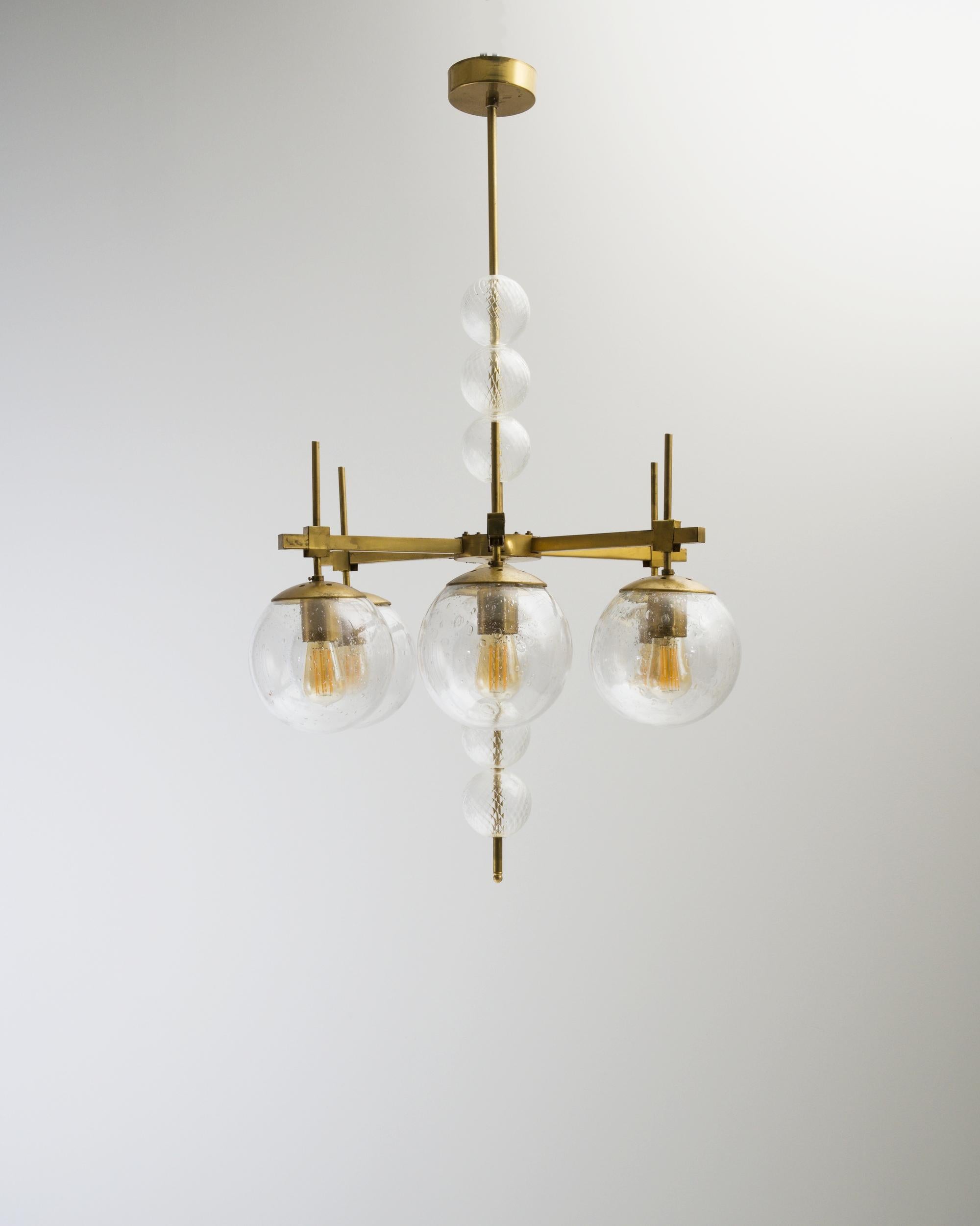 A metal chandelier created in the former Czechoslovakia circa 1970 A unique blend of both mid-century and Art Deco sensibilities, this chandelier combines a sleek construction with a flare for the ornamental. The glass globes that line its center