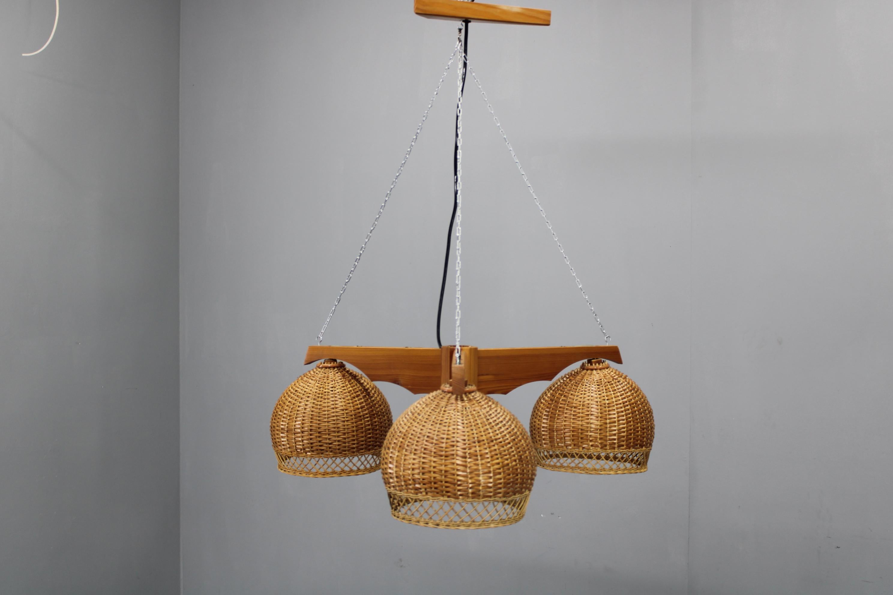 Lampada a sospensione in rattan vintage realizzata in Cecoslovacchia negli anni '70, con tre paralumi in rattan intrecciato a mano, struttura in pino massiccio e sospensione a catena in ferro. 
Questo lampadario scultoreo della metà del secolo