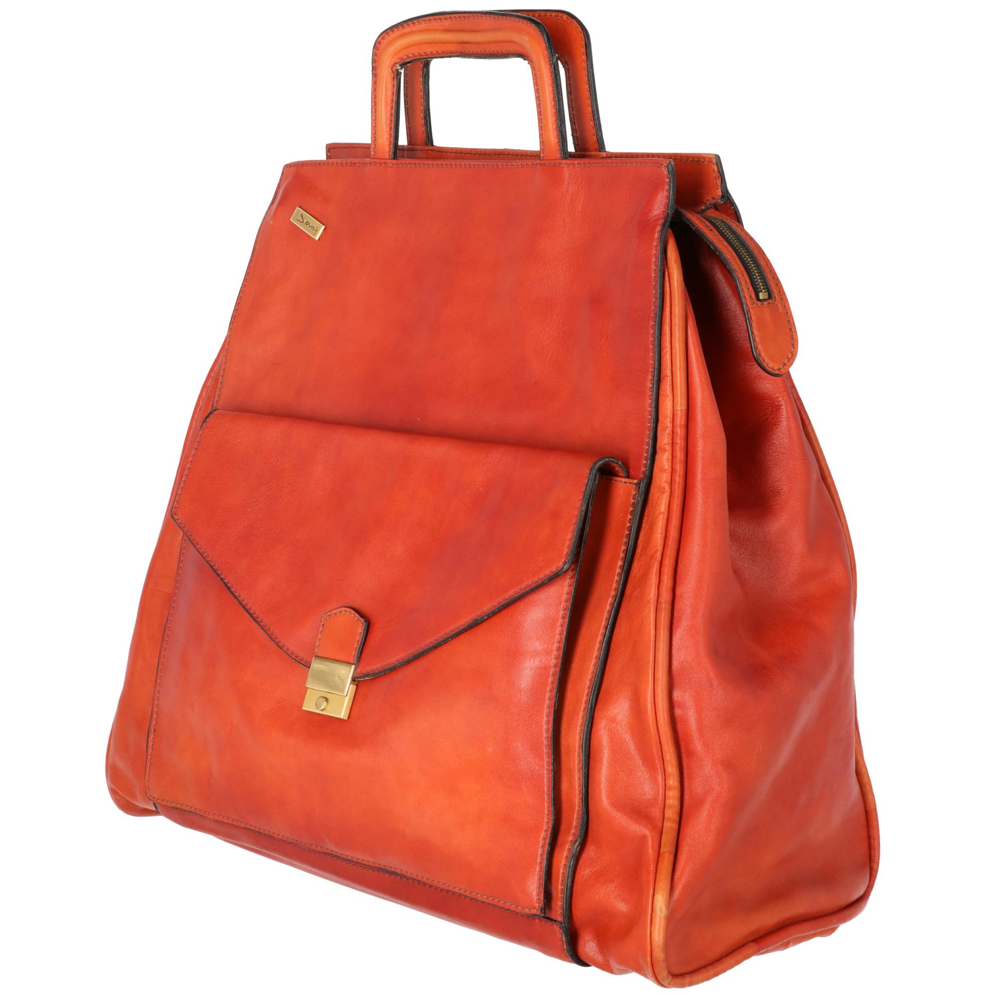 Damy travel bag made of orange leather, with zip closure, two rigid handles, has a pocket with flap and snap closure in golden metal, small front plate in logoed metal. The lining is in military green cotton velvet, has two internal pockets, one