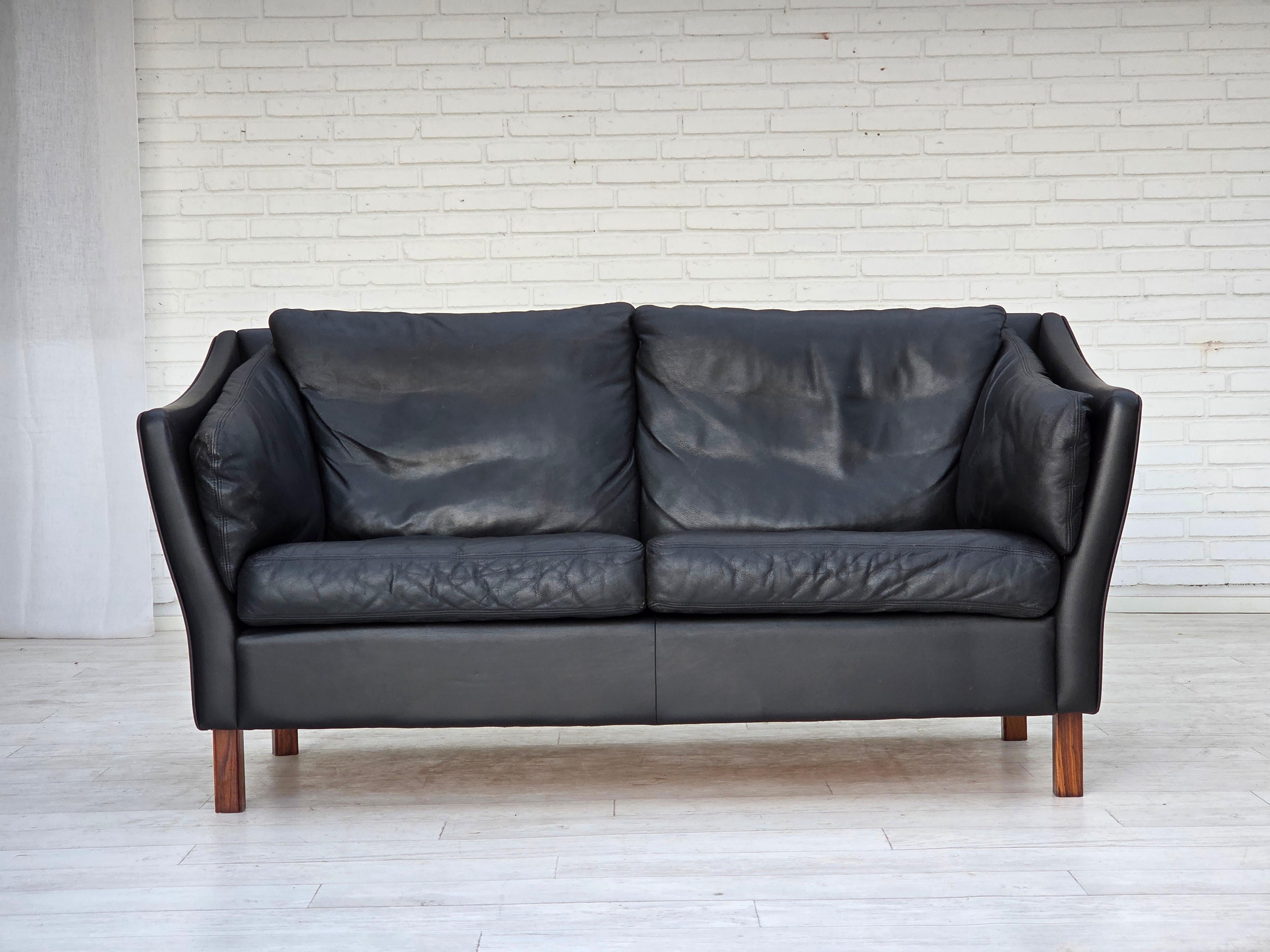 Divano danese a 2 posti degli anni '70. Mobili originali in pelle nera, gambe in legno di teak. Condizioni originali molto buone: nessun odore, nessuna macchia e struttura stabile. Prodotto da un produttore di mobili danese negli anni 1970-75 circa.