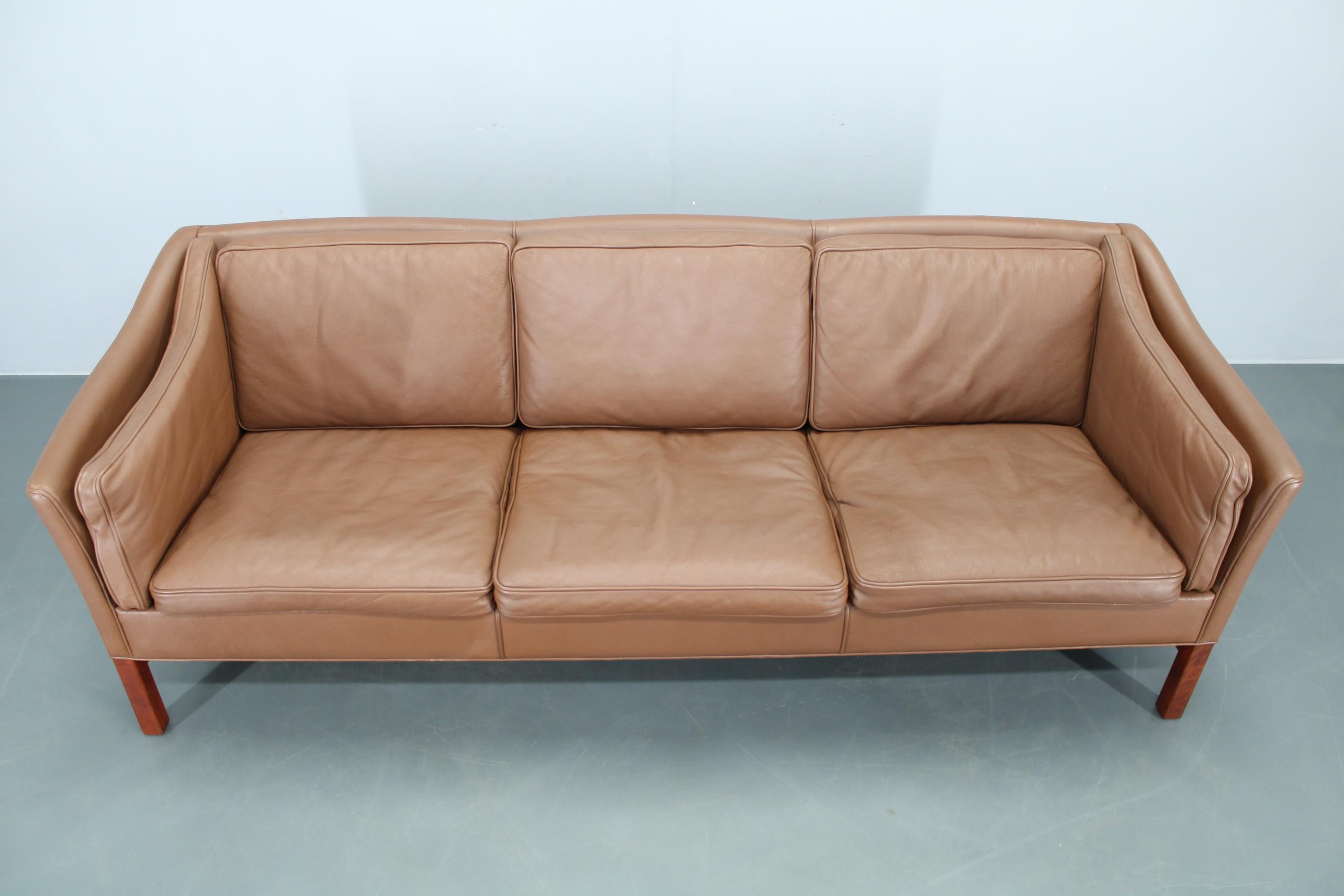 Classico divano danese a 3 posti degli anni '70 rivestito in morbida pelle marrone e sostenuto da una robusta struttura e da gambe in faggio. Questo invitante pezzo vintage è caratterizzato da una soffice imbottitura e da una silhouette senza tempo,