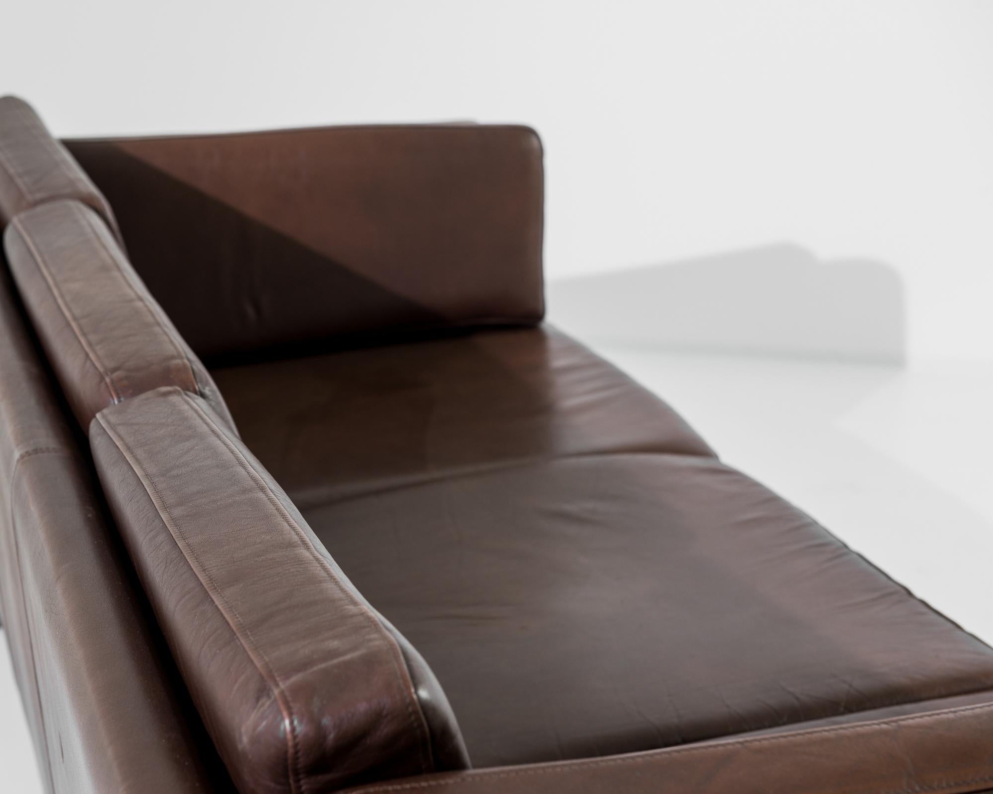 A leather sofa from Denmark, produced circa 1970. A three seat sofa in a rich, chocolate brown leather, standing on four slender square legs. A vintage seat in the Morgensen mold, this piece places a premium on quality of craftsmanship and durable