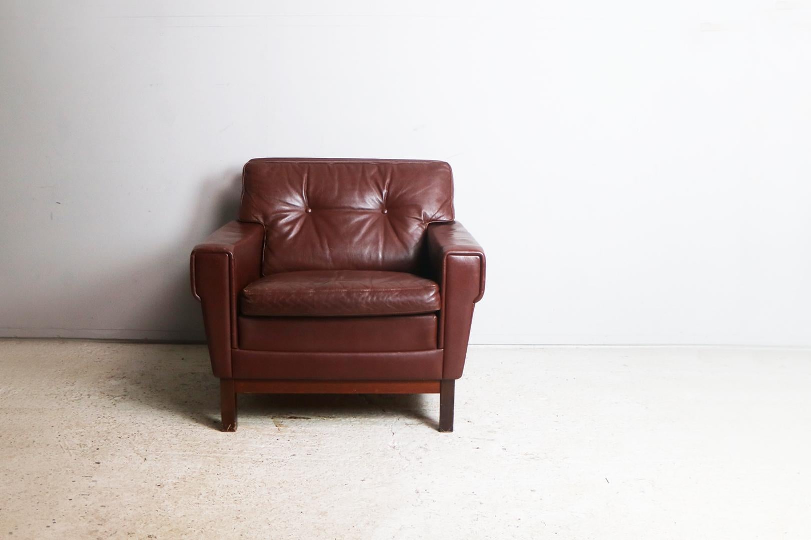A Danish Mid-Century Modern low backed armchair with the original rich brown leather upholstery. Button detailing on the back cushion. Sits on stained beech feet.
    