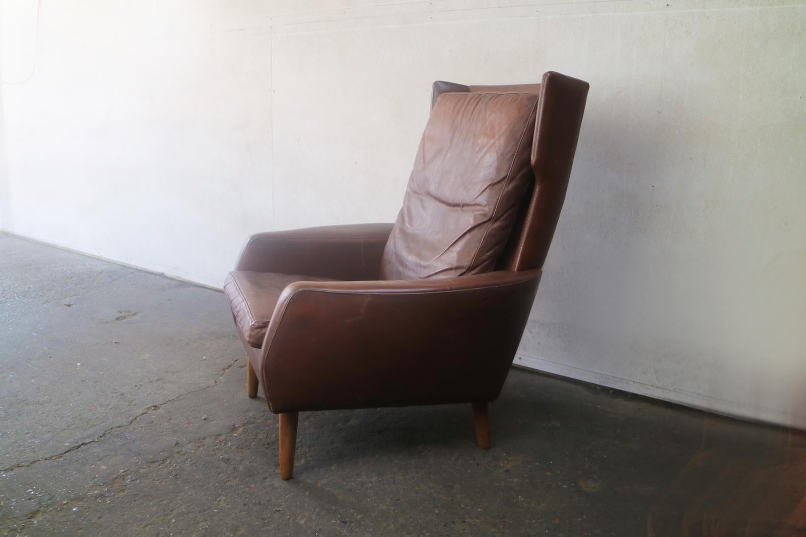 A Danish 1970s armchair, with the original brown leather upholstery. A very high back with side ’wings’ towards the top. Sits on turned teak legs.
   