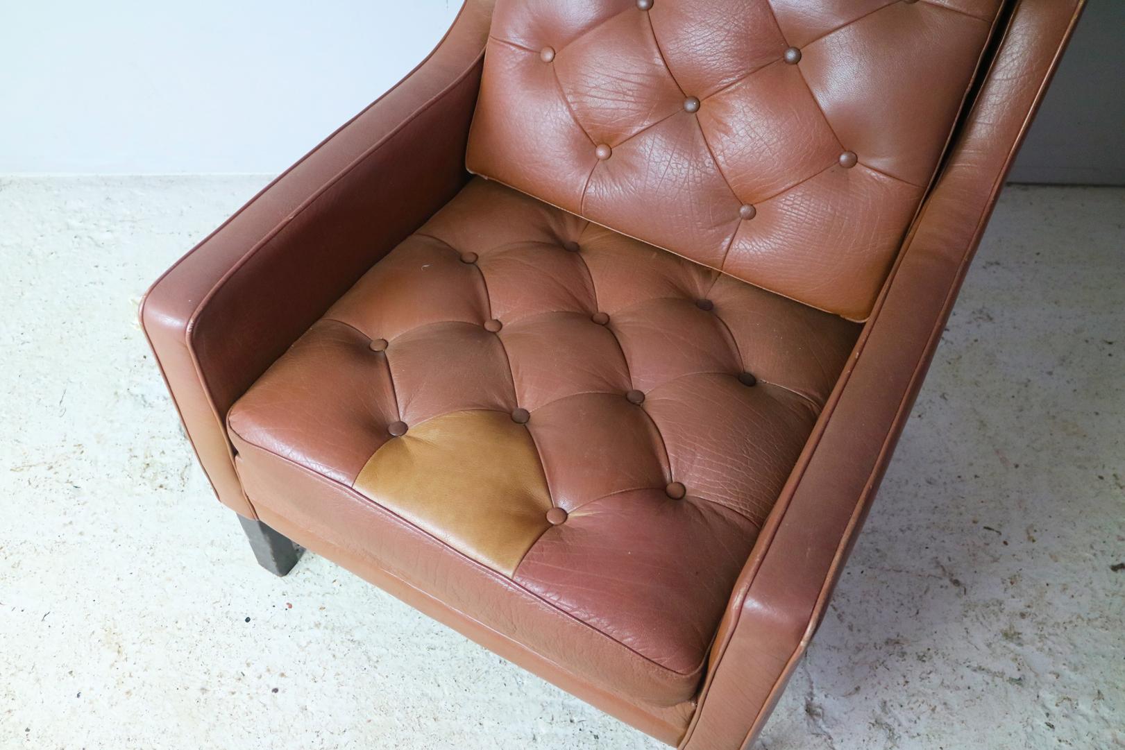 A Danish Mid-Century Modern low backed armchair. The original leather upholstery is quilted with button detailing. A nice feature is the lighter leather triangle that appears at the front of the seat cushion. Sits on stained beech feet. 
 