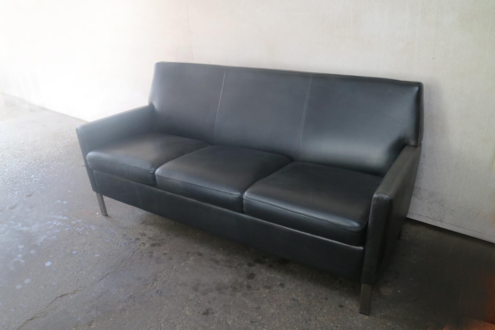 A late 1970s three-seat sofa with original black leather upholstery and brushed steel legs.