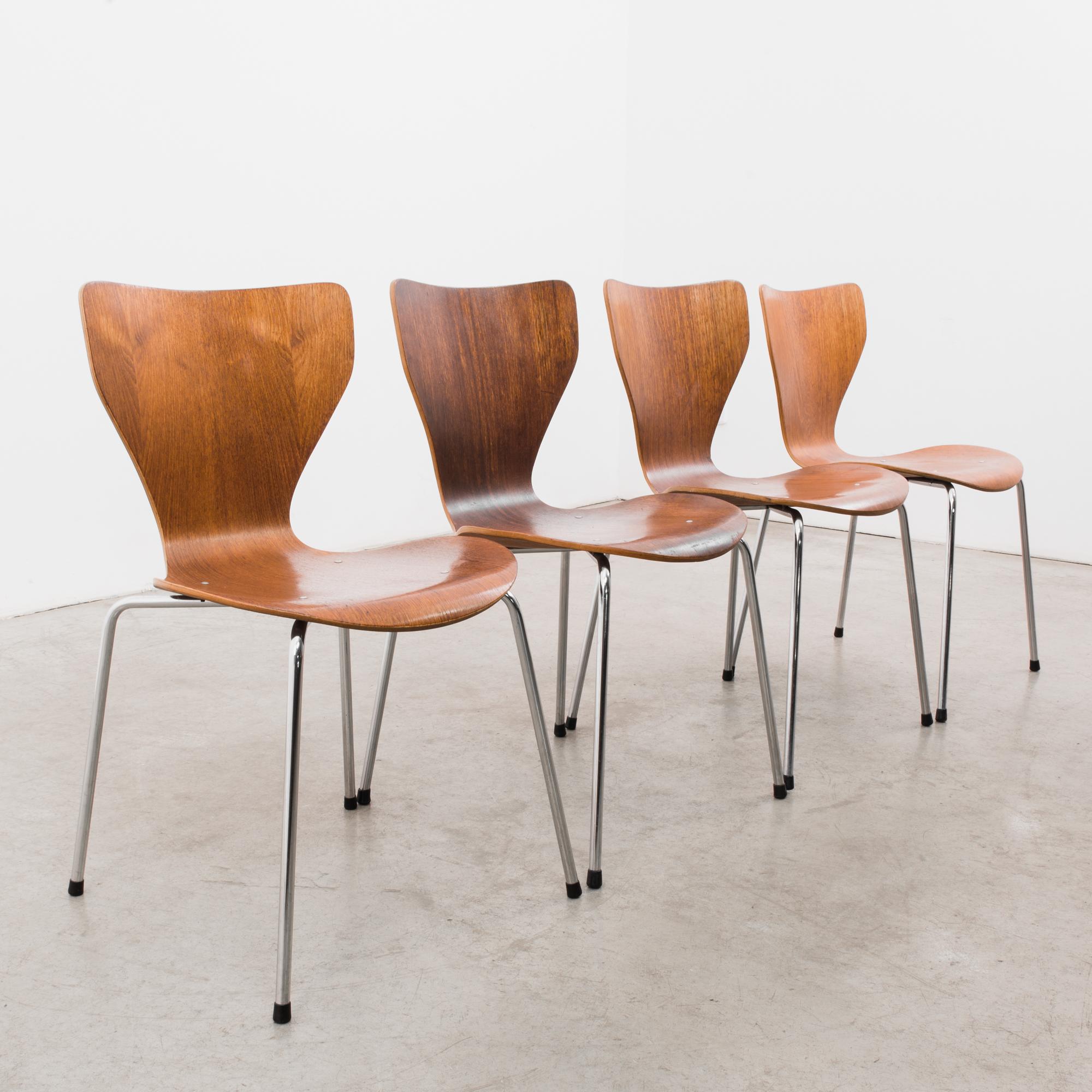 A set of four wooden dining chairs from Denmark, circa 1970. A modern, abstract design; a seat of bent plywood sits upon four slender silver legs. The plywood’s thinness contrasts with the fullness of the silhouette it creates, a fluid, wasp-waisted