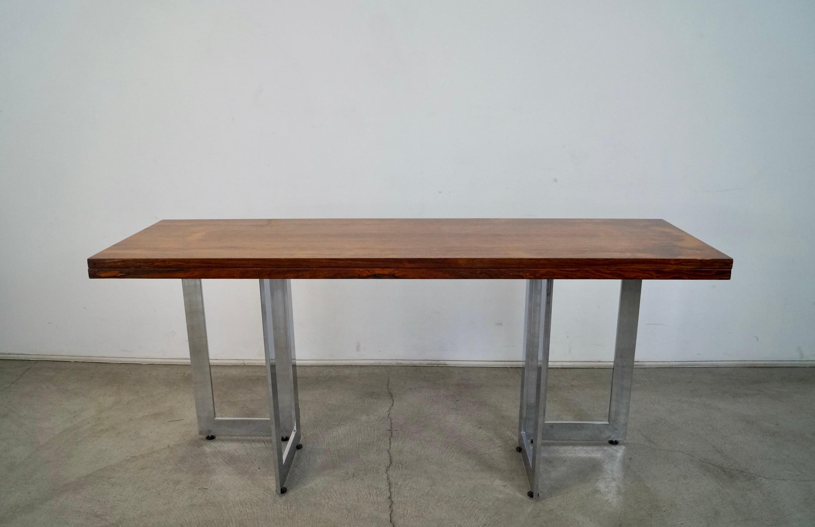 Vintage 1970's Midcentury Modern extendable table for sale. Can be used as a console table, writing desk, or dining table. It has been professionally refinished, and is now immaculate. The chrome has been polished. It's made of rosewood with a