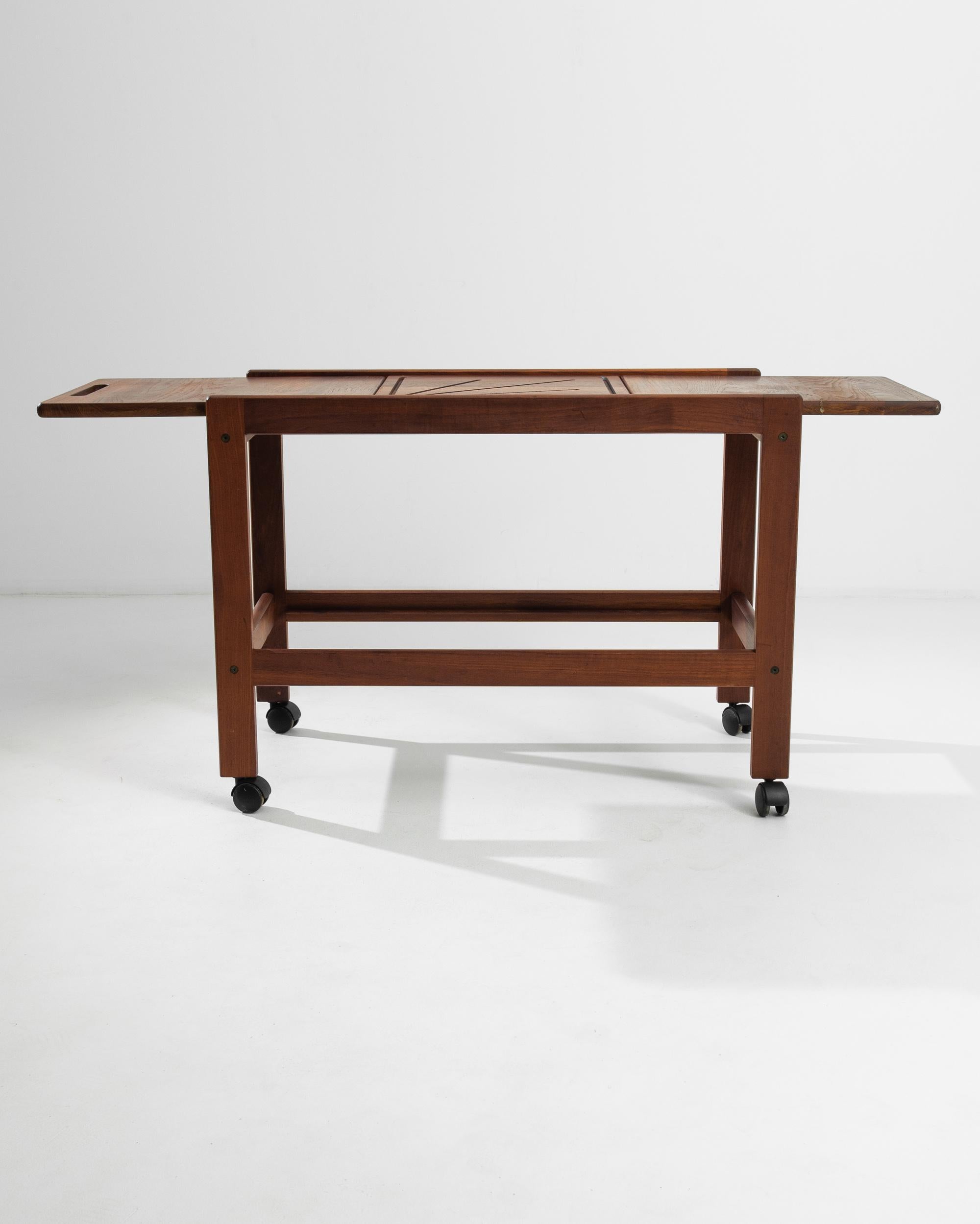 Laying a full focus on minimalism and functionality, this Danish teak cart features a simple two-tier structure resting on caster wheels. Rearrangeable trays give a variety of configurations. The smooth corners and rich finish animate the masterful