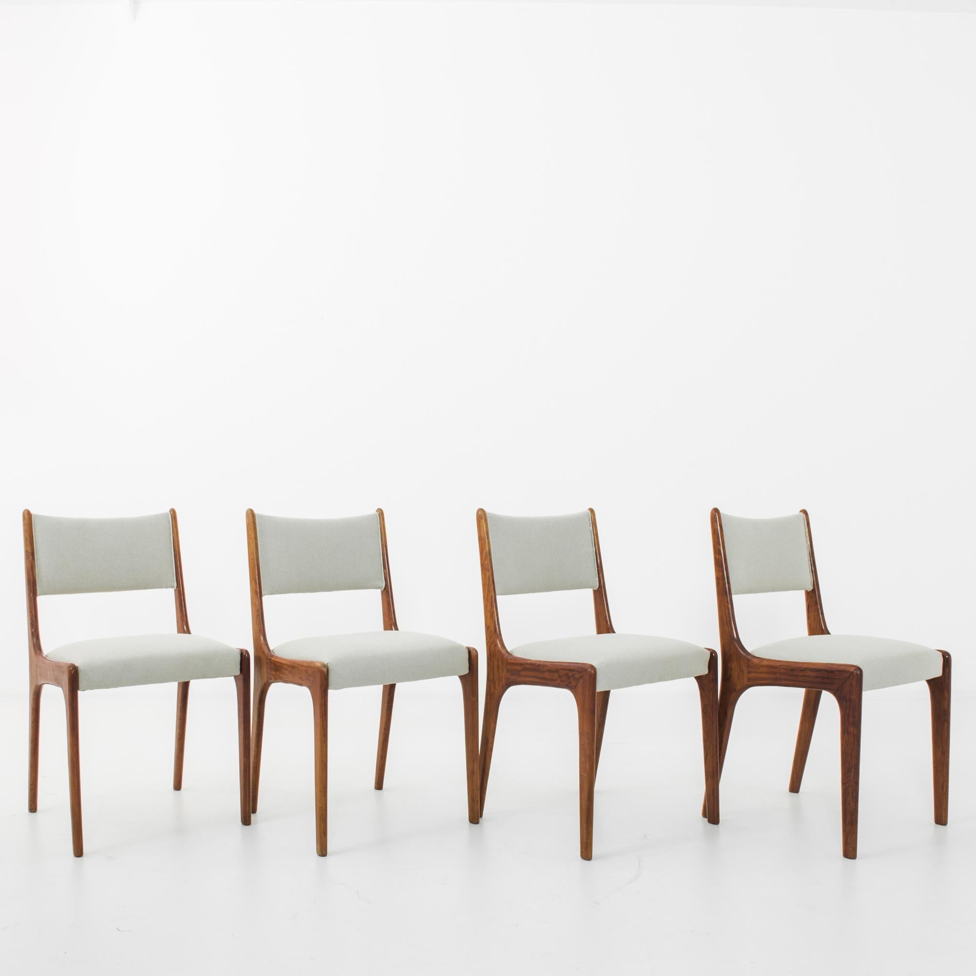 A teak dining chair set in characteristic mid-20th century Danish style. Simple forms combine dynamically, at angles with reclining back and supportive legs. The re-upholstered seat hovers within the wooden frame, the warm polished teak