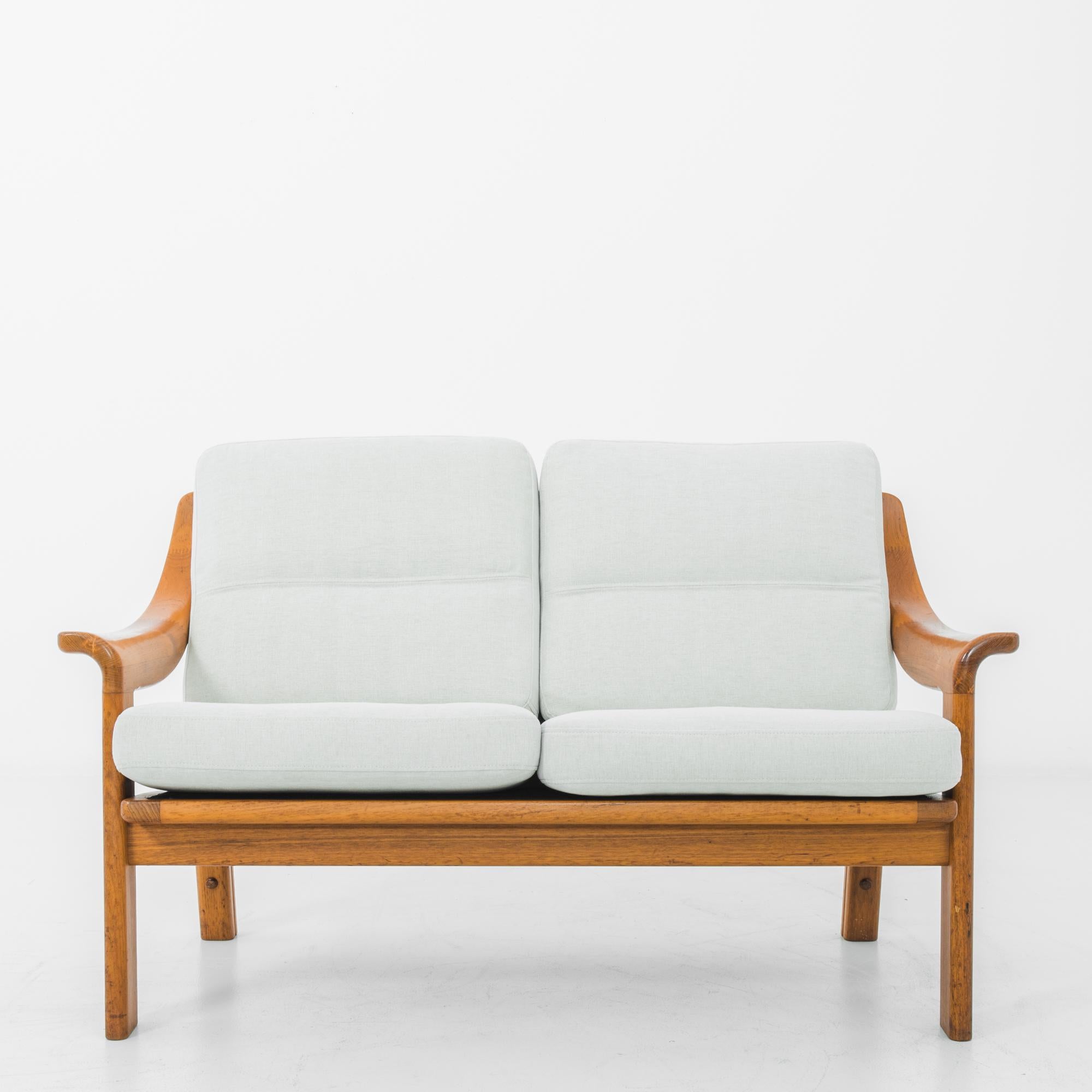 This two-seat teak sofa was made in Denmark, circa 1970. Rounded edges and the sleek curves of the armrests reflect the simple elegance of Danish Modern design. The newly upholstered seat and back feature an eggshell tint, complementing the golden