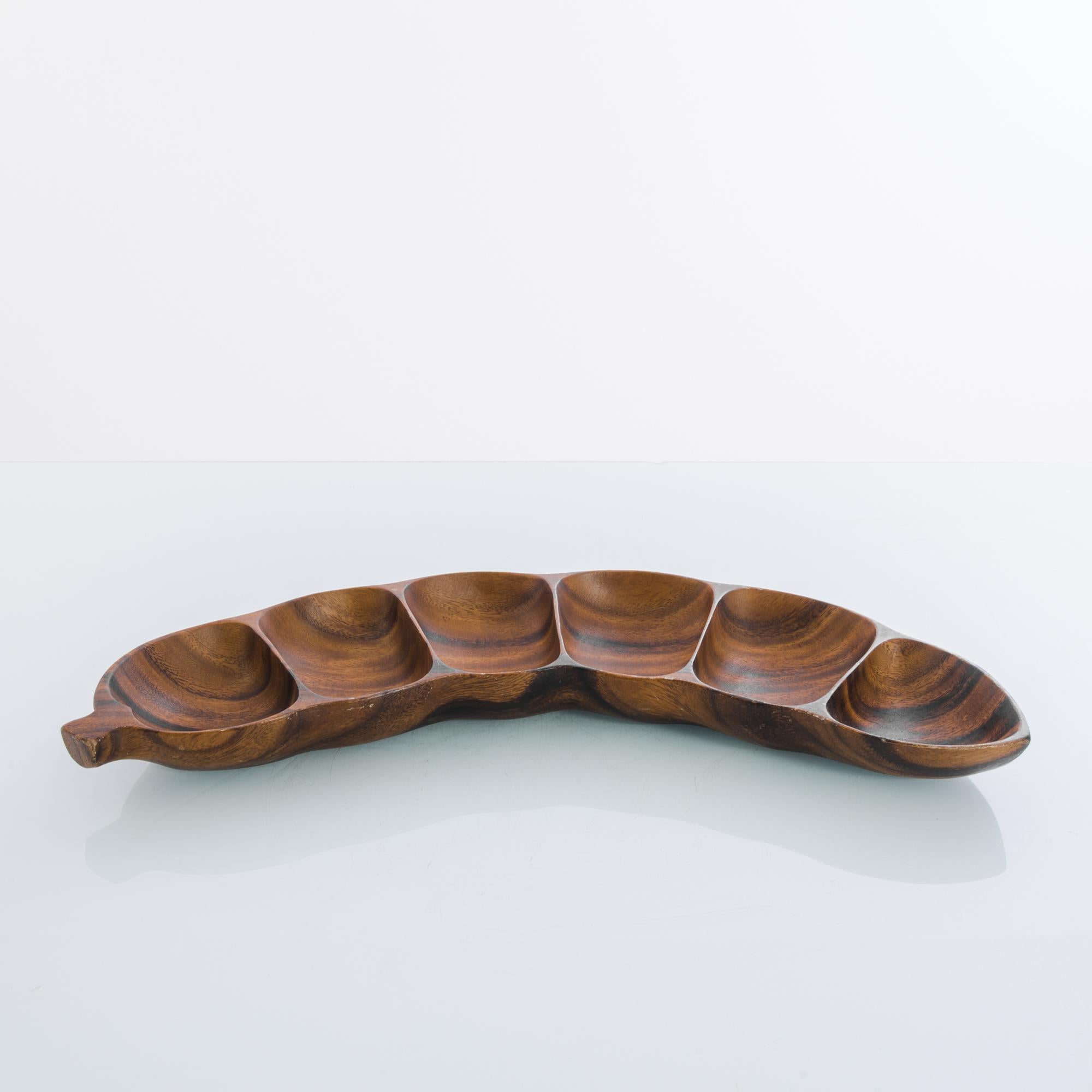 A wooden bowl from 1970s Denmark in the shape of a bean pod. The six partitions of the bowl mimic the natural form of the bean; the wood has a rich color with warm reddish tones and a dark grain, brought out by a fine polish. The unique shape and