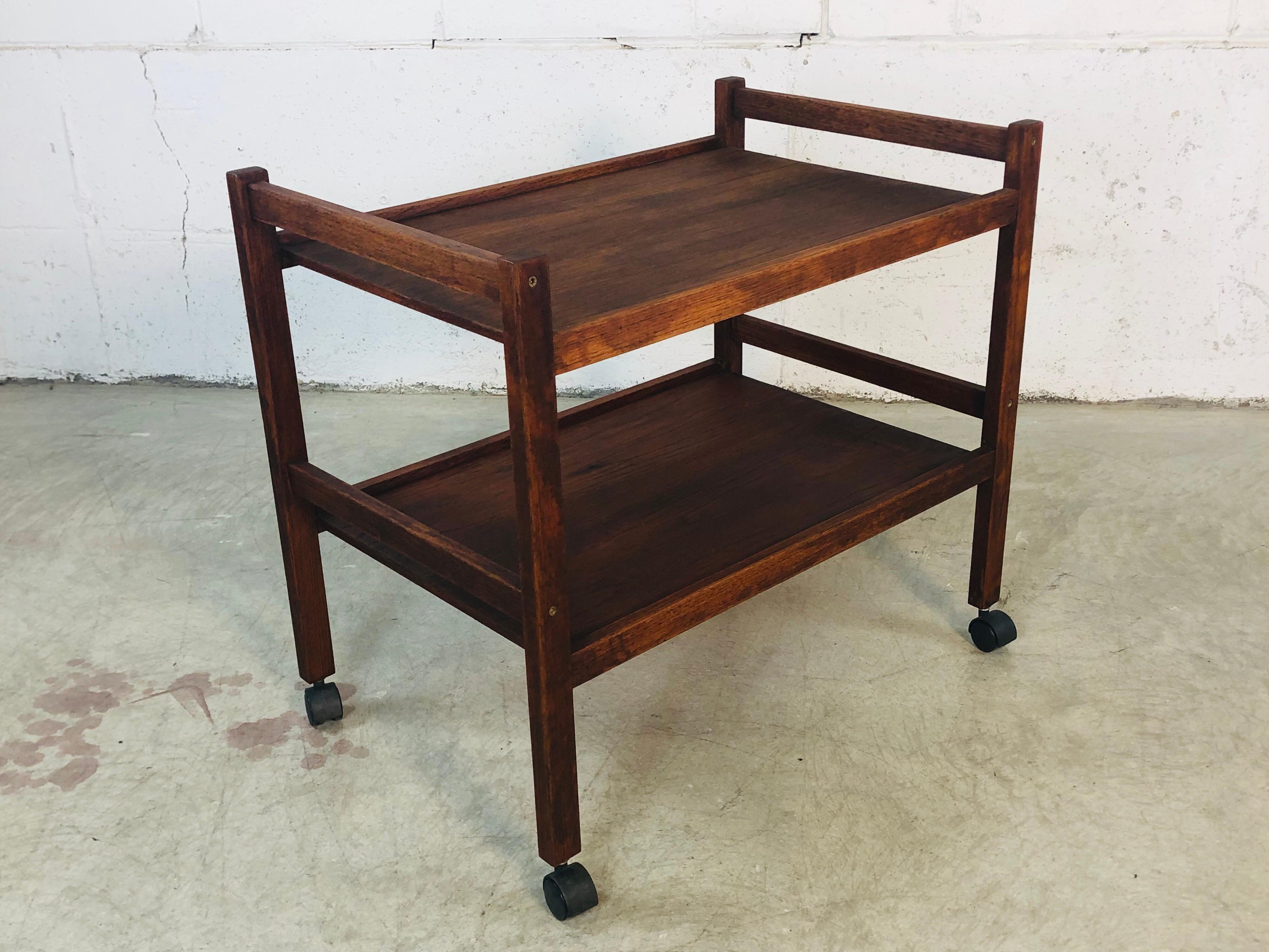 Vintage 1970s Danish dark teak wood rolling cart. The cart has two shelves for storage and rolls freely. The cart is in excellent refinished condition. No makers mark.