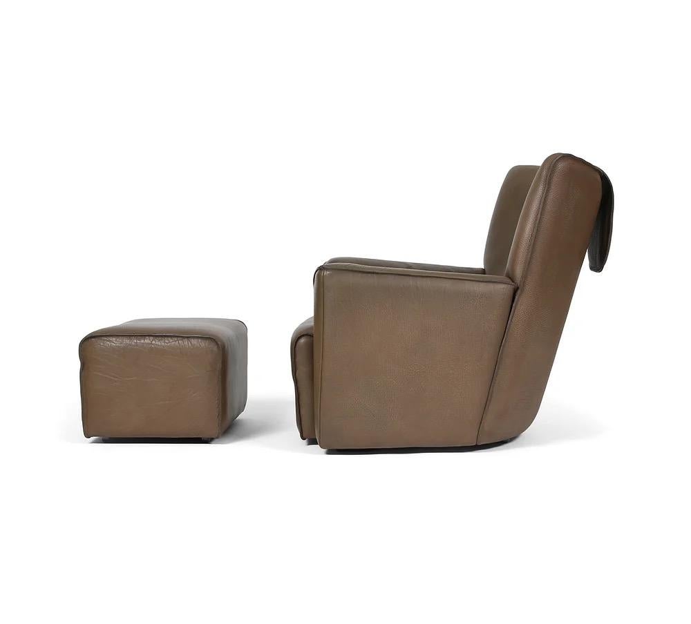 Here is a vintage 1970s de Sede lounge chair with ottoman in thick and soft brown leather. This line of seating was designed by Robert and Trix Haussmann and included low, mid, and high back chairs and sofas. This is the high-back version, which