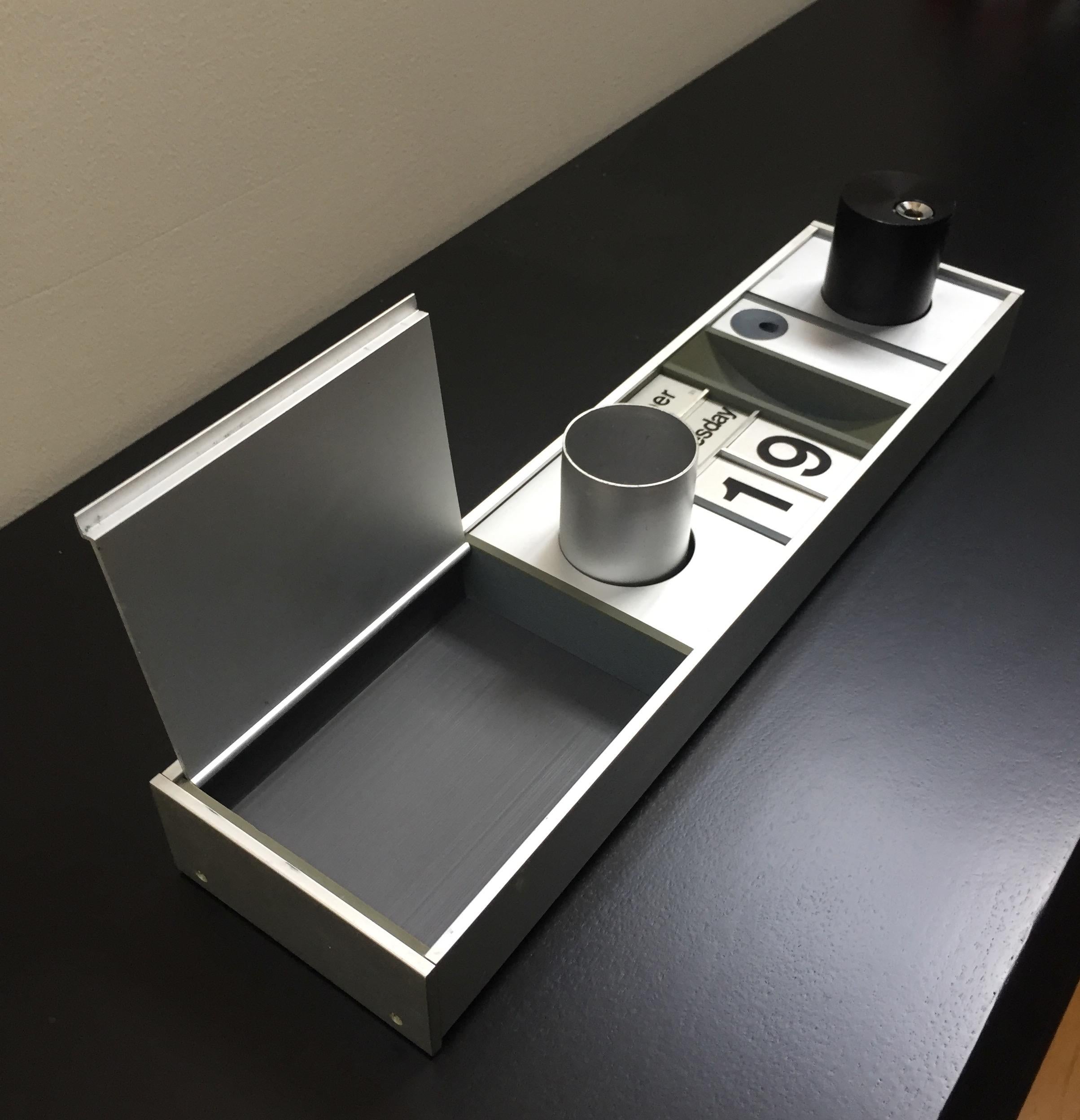 This aluminium desk organizer manufactured by Frank Guille and Frank Height in the 1970s has a covered compartment, calendar, pen cup, Dieter Rams lighter, and space for paper clips and pen holder.