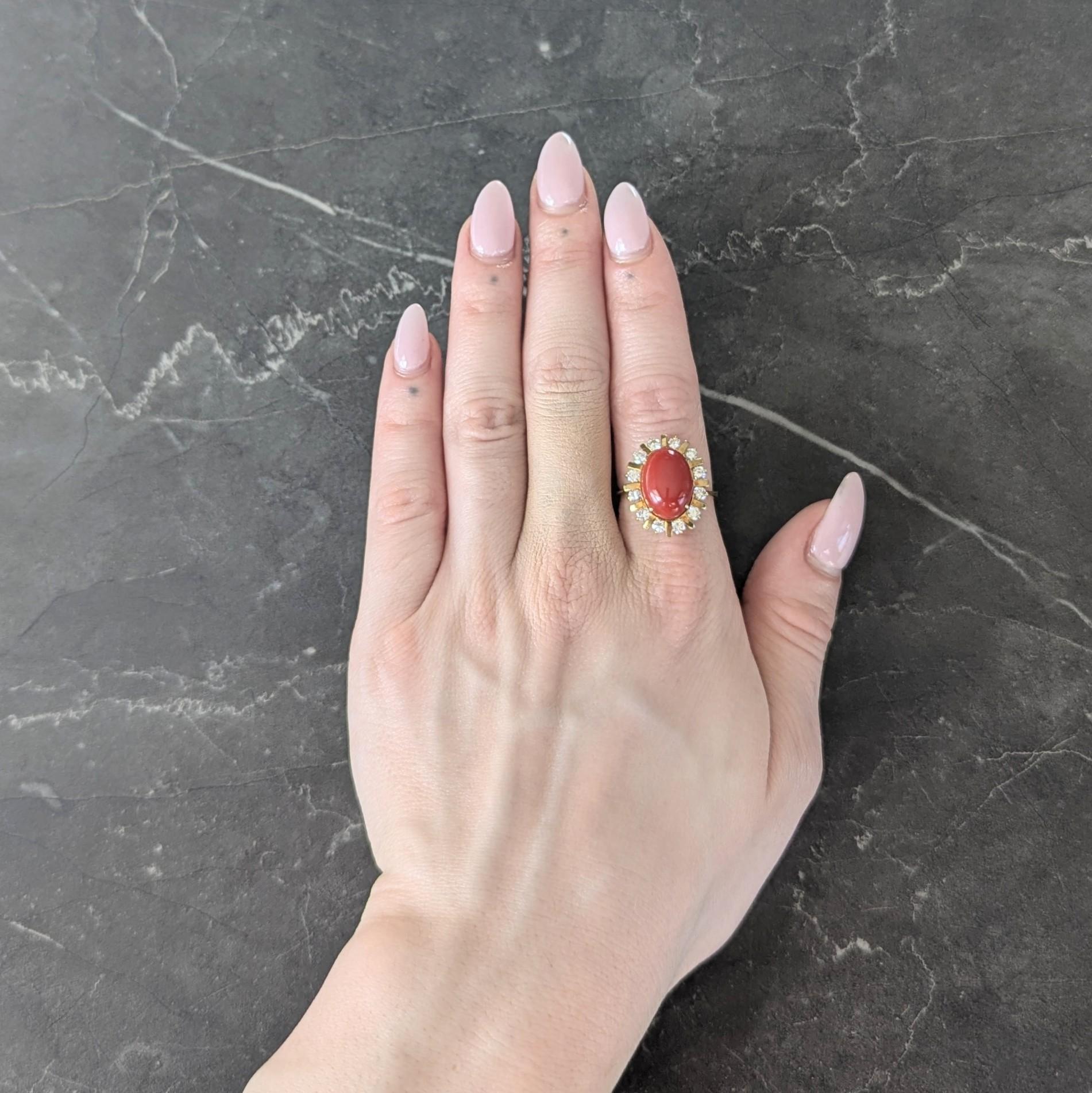 Centering an oval shaped coral cabochon measuring 10.0 x 14.0 mm
Opaque medium orangey red in color - prong set in a wire basket
Accented by a fanning radial surround with a prong set diamond halo
Round brilliant cut and weighing approximately 0.72