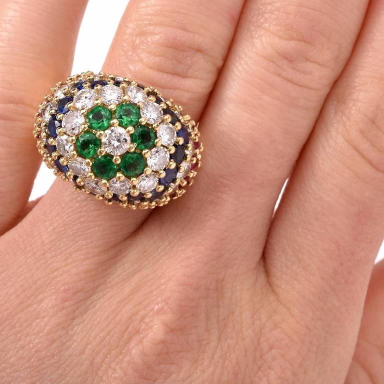 This fashionable circa 1980's Estate Retro cocktail ring is crafted in solid 18K yellow gold. It is designed as a dome shape plaque, adorned with genuine high quality diamonds, rubies, emeralds and sapphires. The vividly colored genuine Emerald,