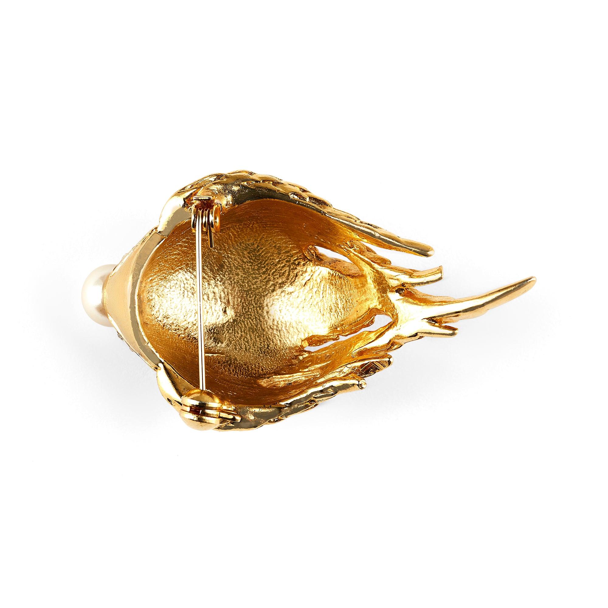 Cette broche en forme de coquillage de CIRCA, datant des années 1970, attire l'attention. Méticuleusement fabriquée en métal plaqué or 22ct, la broche est ornée de sections gravées. Une fausse perle est posée sur le dessus, entourée d'un piédestal