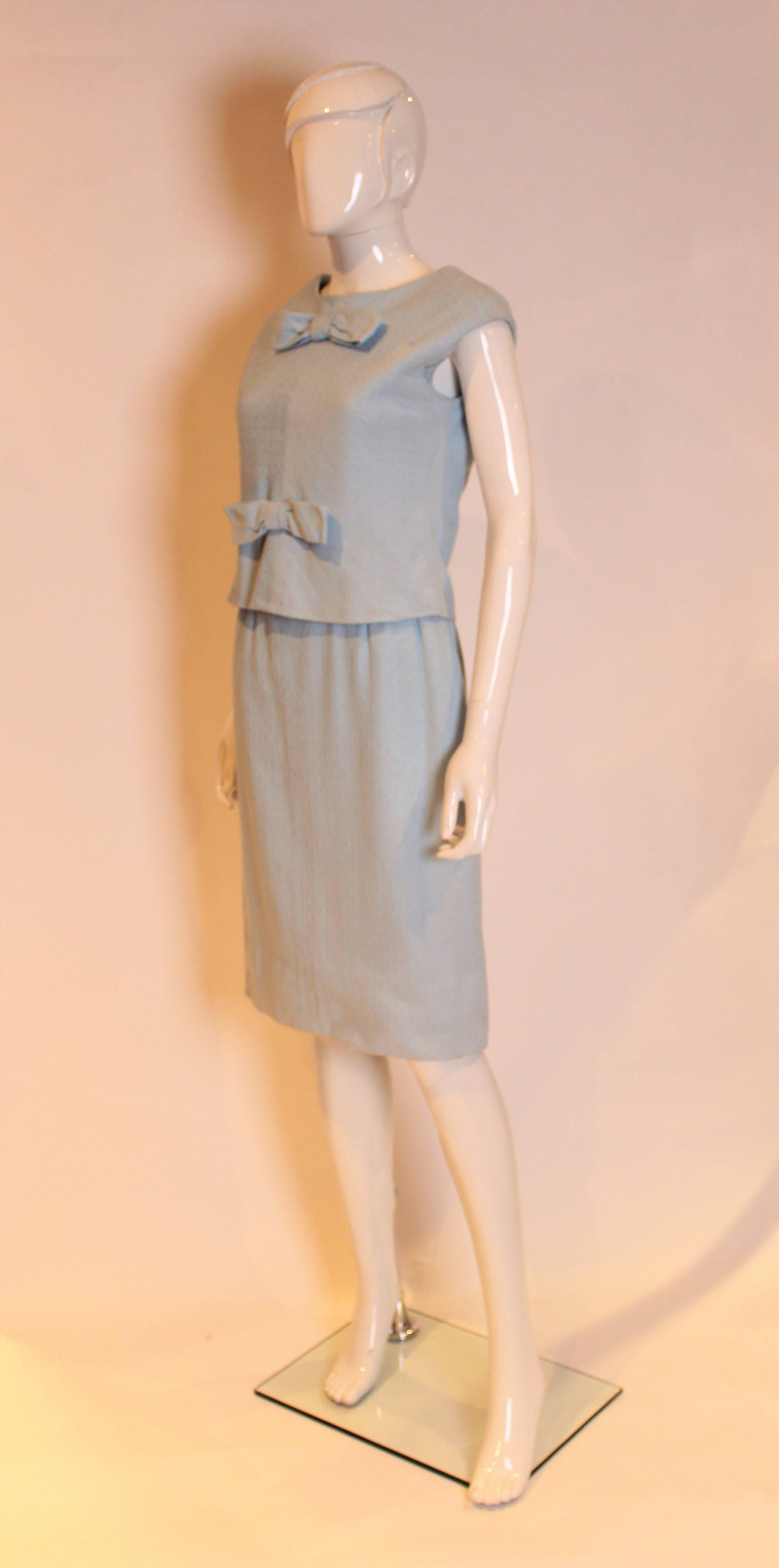 A chic dress by Yves Saint Laurent ,made for the British department store, Fortnum and Mason. In textured light blue wool, the dress has a removeable shell top with four button back and two bows on the front. The under dress has a shift top with