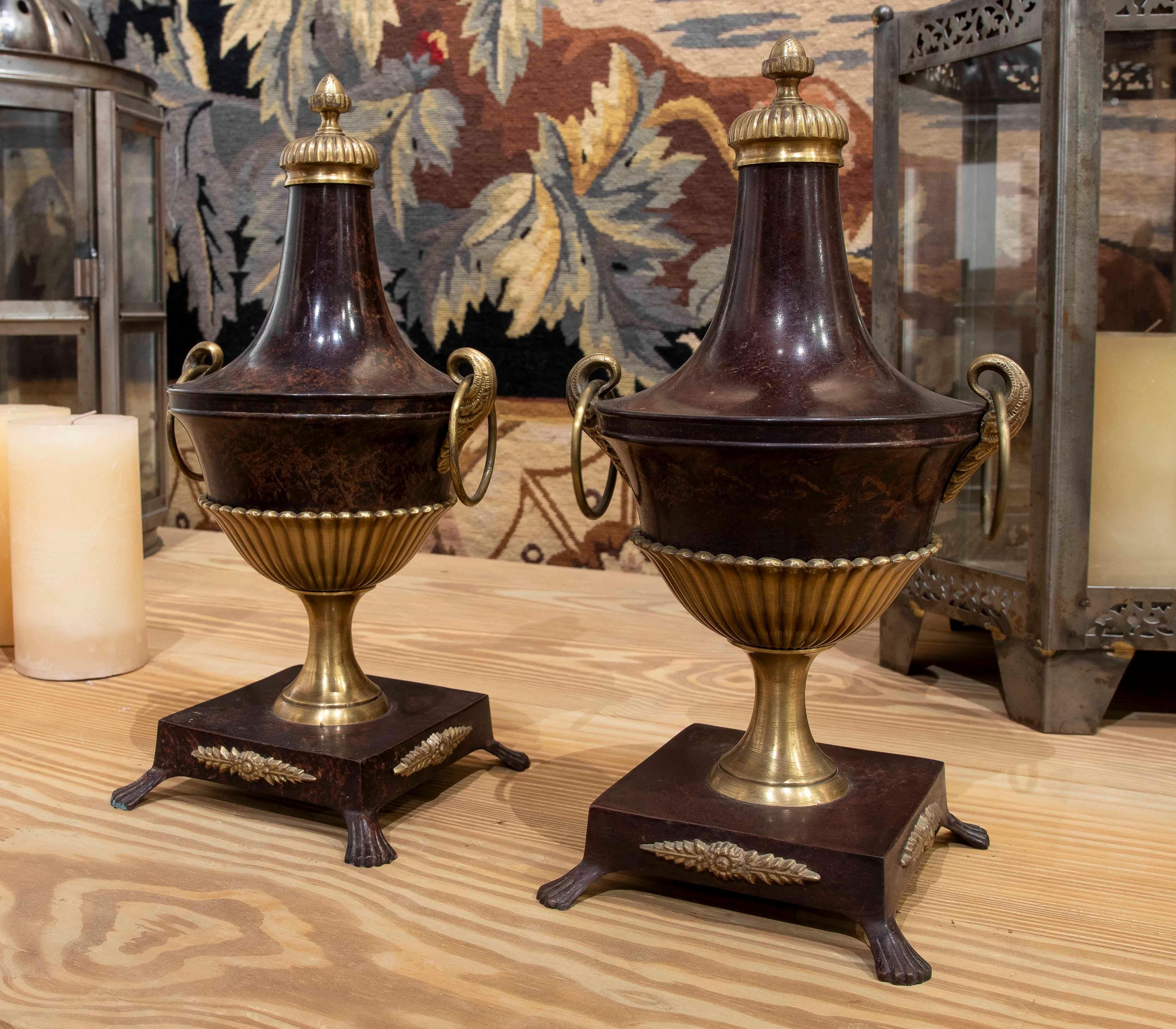 Bellissima coppia di tazze decorative in bronzo con finitura marrone scuro e dettagli dorati. Il suo design sofisticato combina raffinate forme curve con maniglie laterali a forma di serpente, evocando il lusso dell'antichità classica. La base