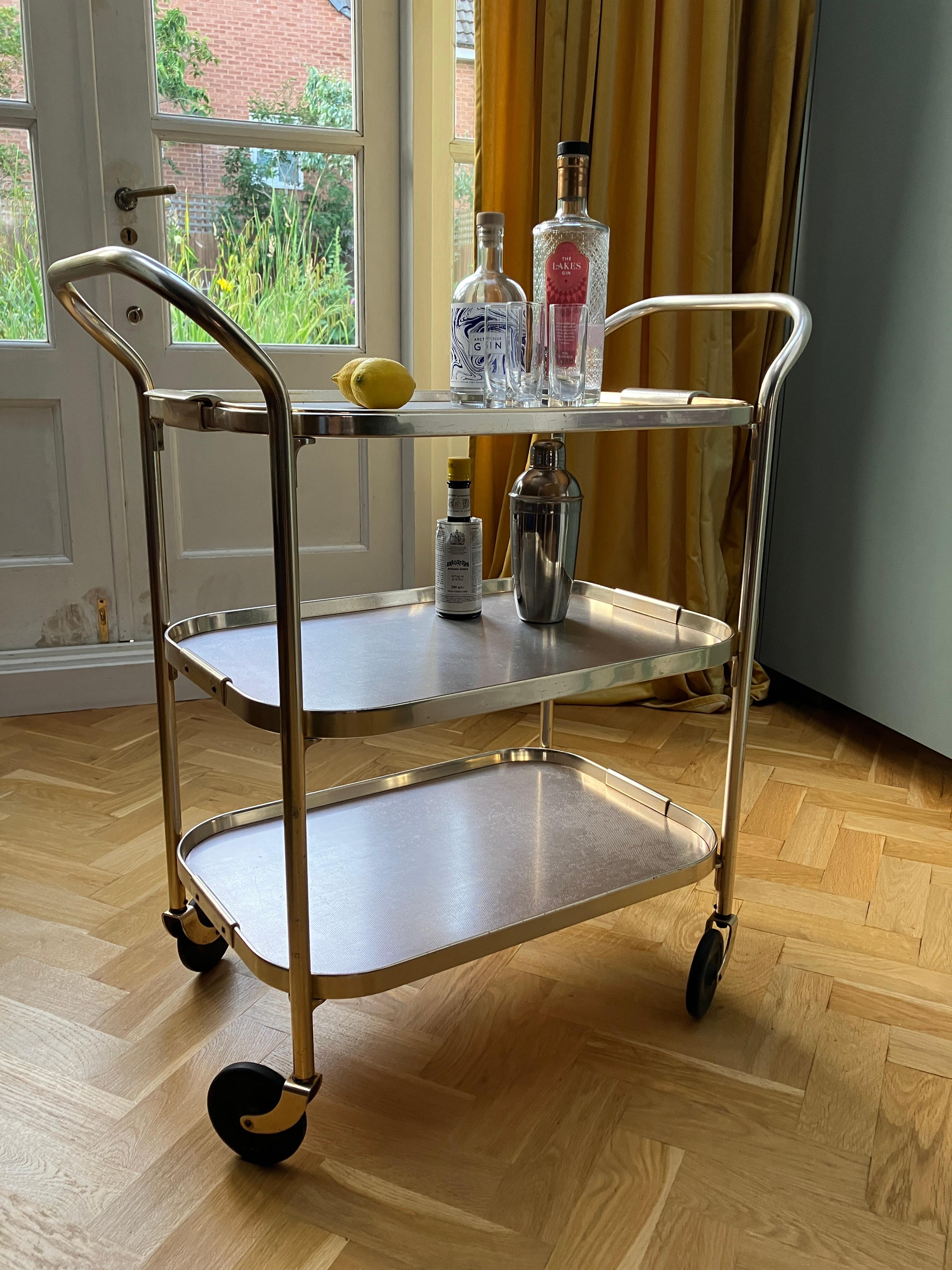 A very nice vintage serving trolley with three tiers. The top tray is separate and can be used as a serving tray. 

The drinks trolley is made of aluminium, and has a luxurious ionized rose gold colour finish. The trolley has attractive black