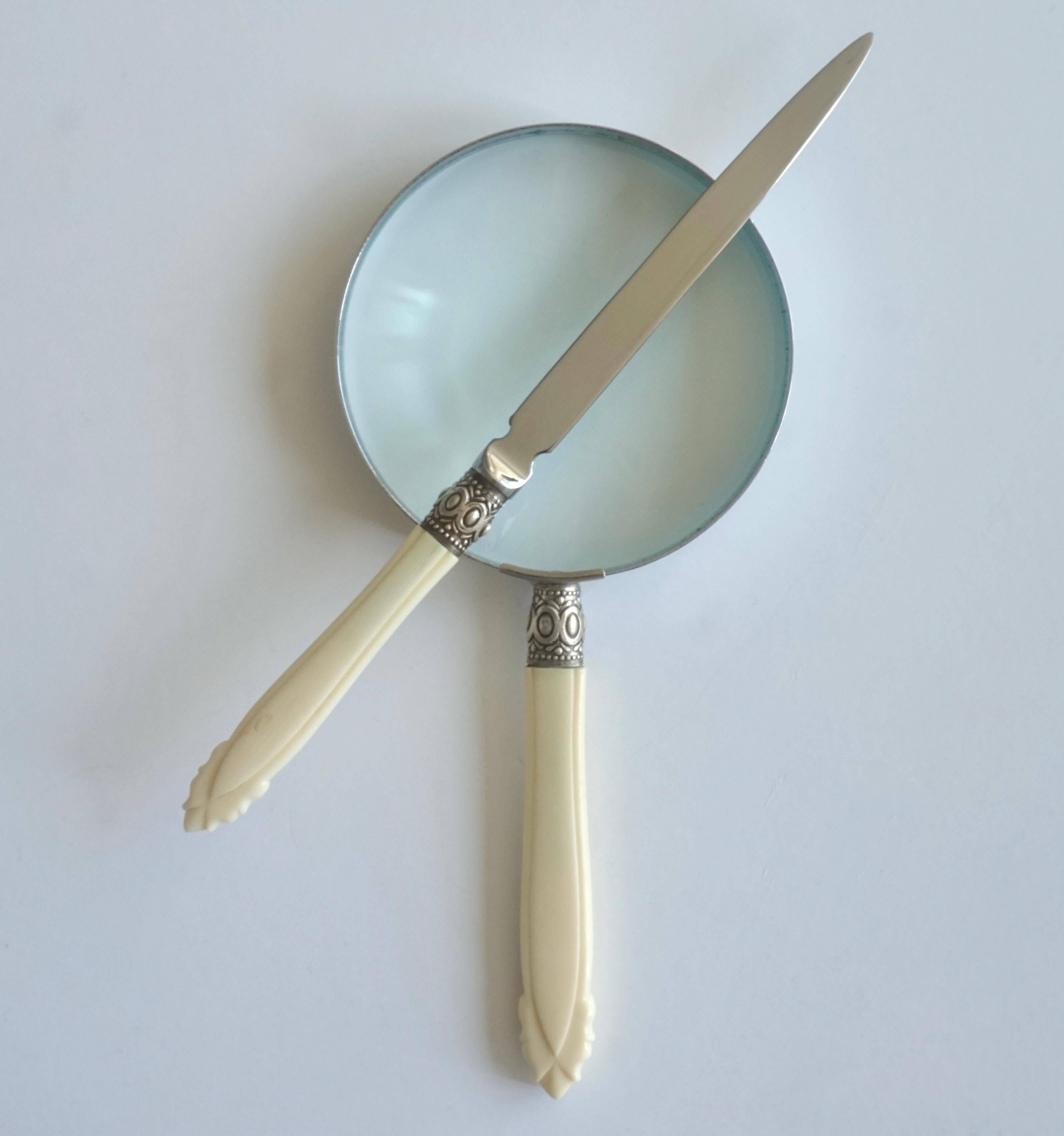 A vintage Mid-Century Modern desk accessory set composed of an Art Deco style magnifying glass and a letter opener with hand-carved bone handles mounted with a silver plated handcrafted chased organic decor, with geometric pattern, supporting the