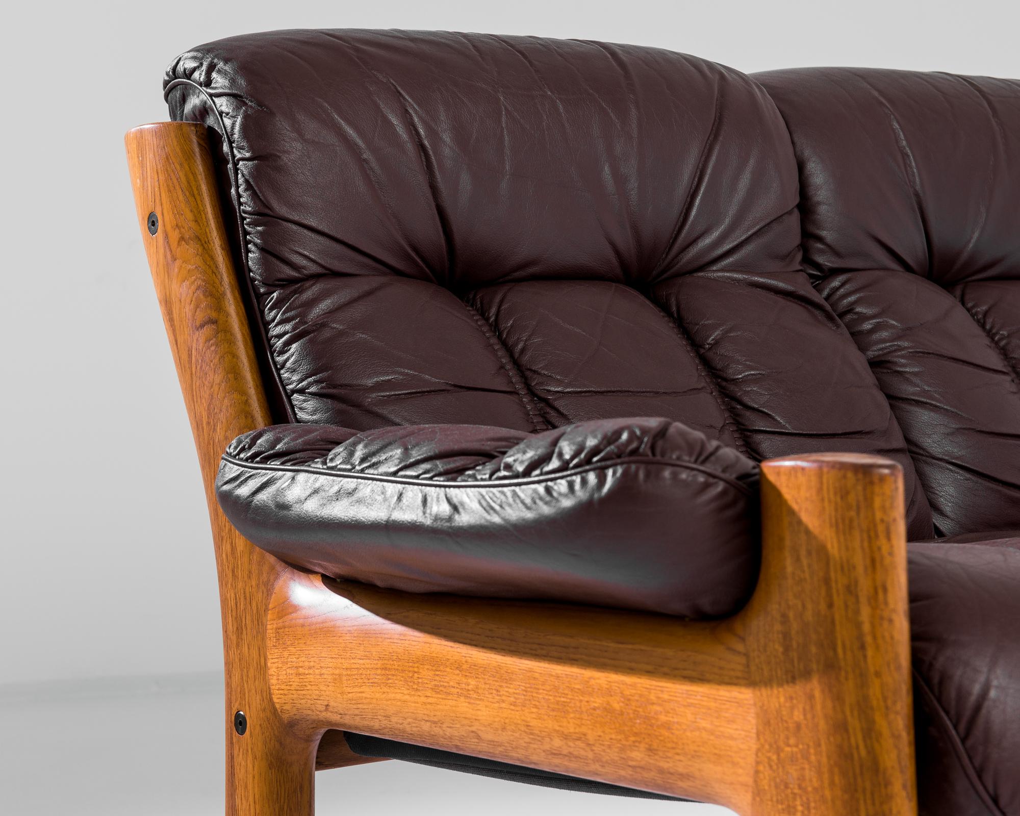A 1970s sofa by Norwegian furniture designer Ekornes. Double cushions create an inviting loveseat of bright teak and rich oxblood leather. The rounded curves of the teak frame echo the organic line of tree branches, while the sophisticated